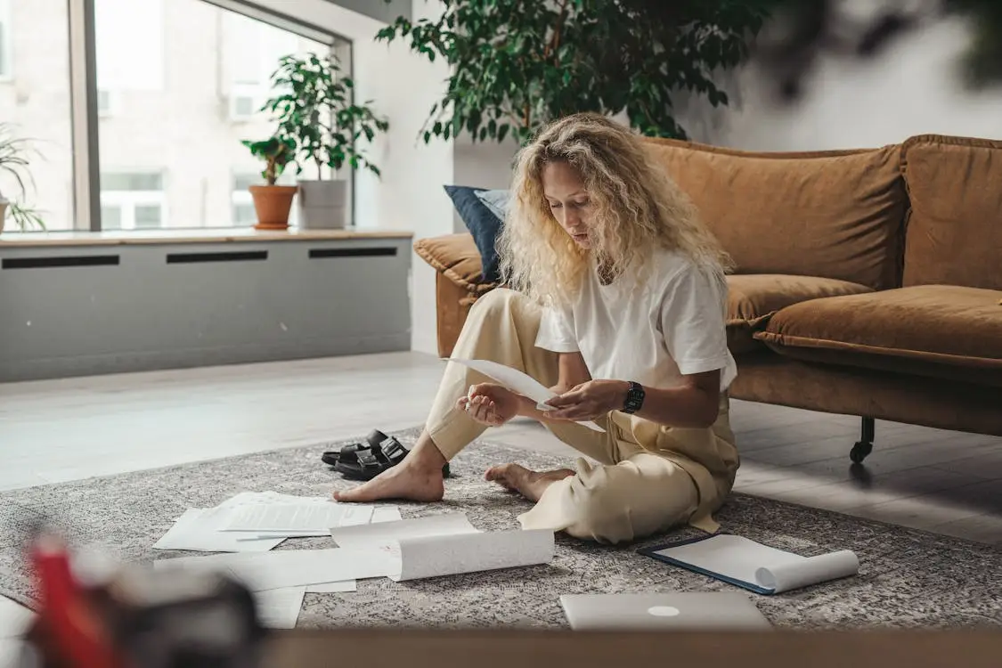 Person sitting on a living room floor reviewing documents with a brown sofa in the background