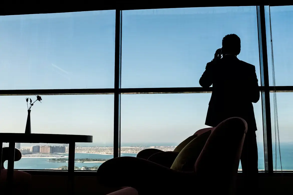 Silhouette of man on phone by large window overlooking cityscape and ocean