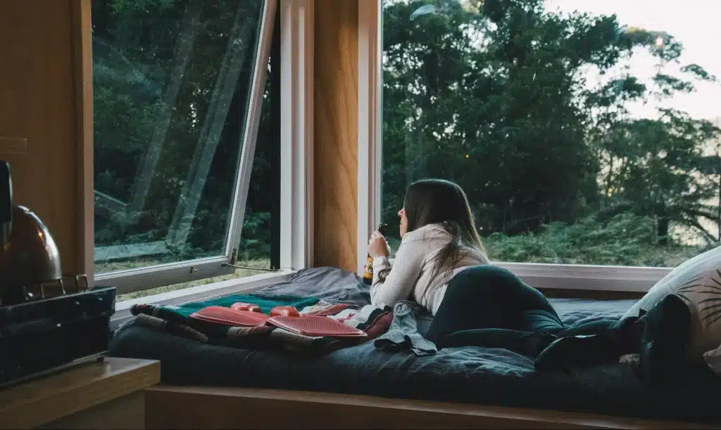 Woman relaxing on window seat with drink in cozy cabin overlooking forest scenery