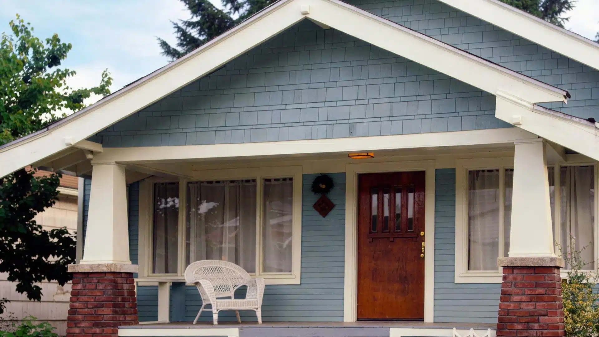 A small blue house featuring a porch, surrounded by greenery
