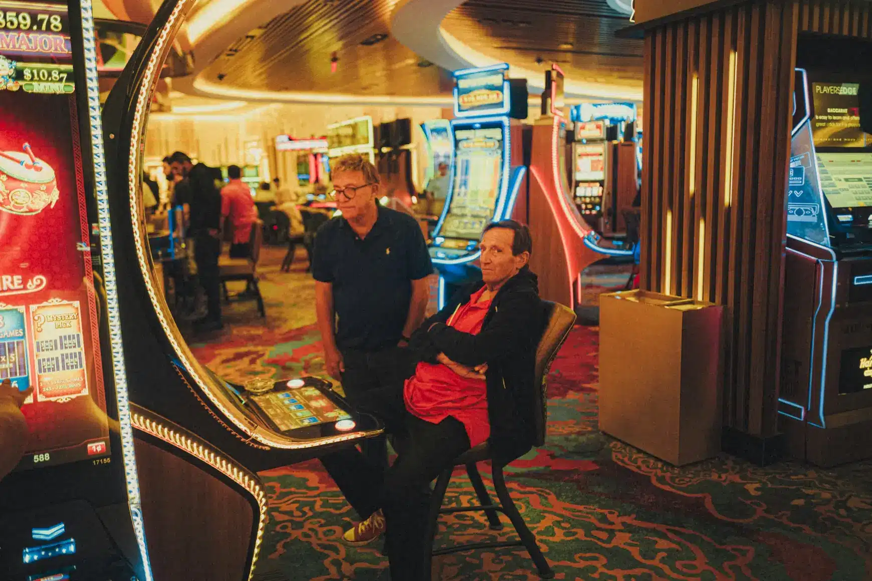 Two men watching slot machine games in a brightly lit casino setting