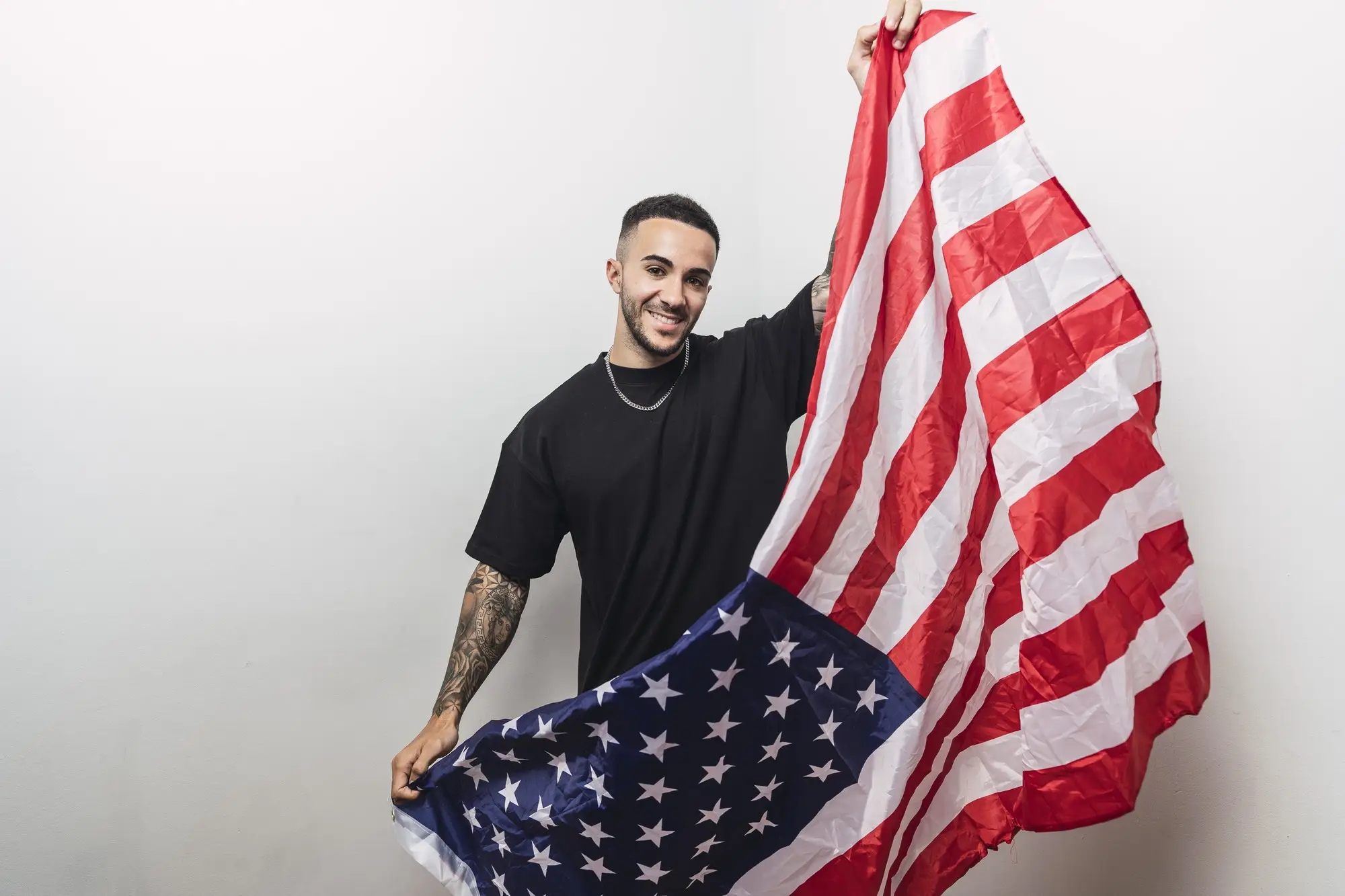 Man holding an American flag in plain white indoor setting