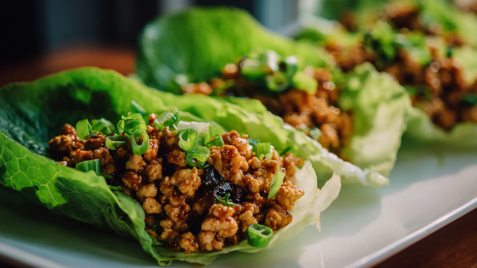 Center focused Asian ground chicken lettuce wraps in crisp romaine leaves garnished with chopped green onions in wooden platter
