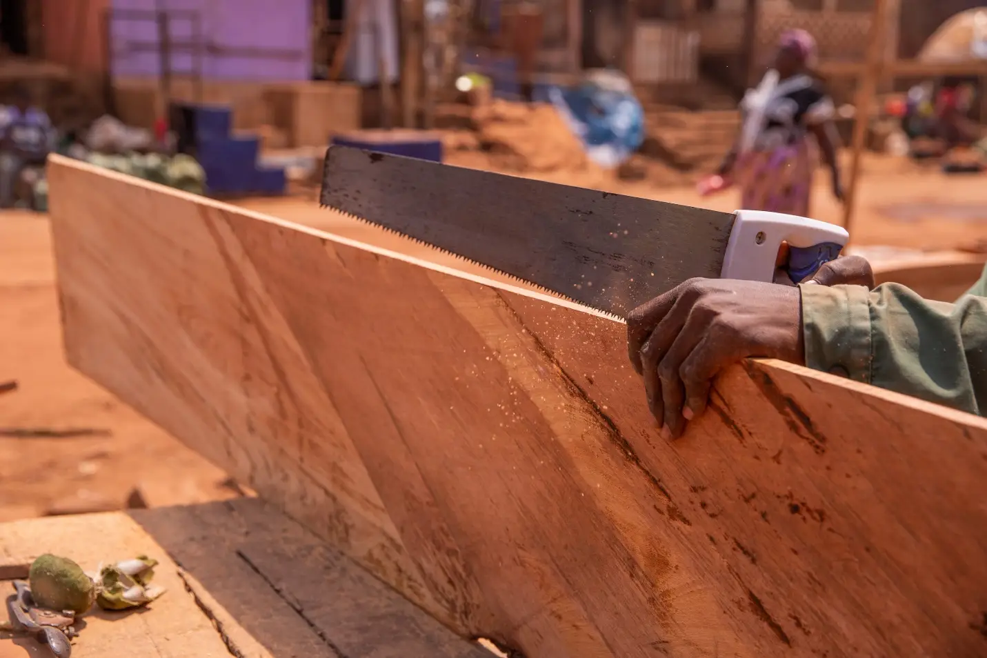 Hand sawing a wooden plank outdoors in a sunlit workshop setting