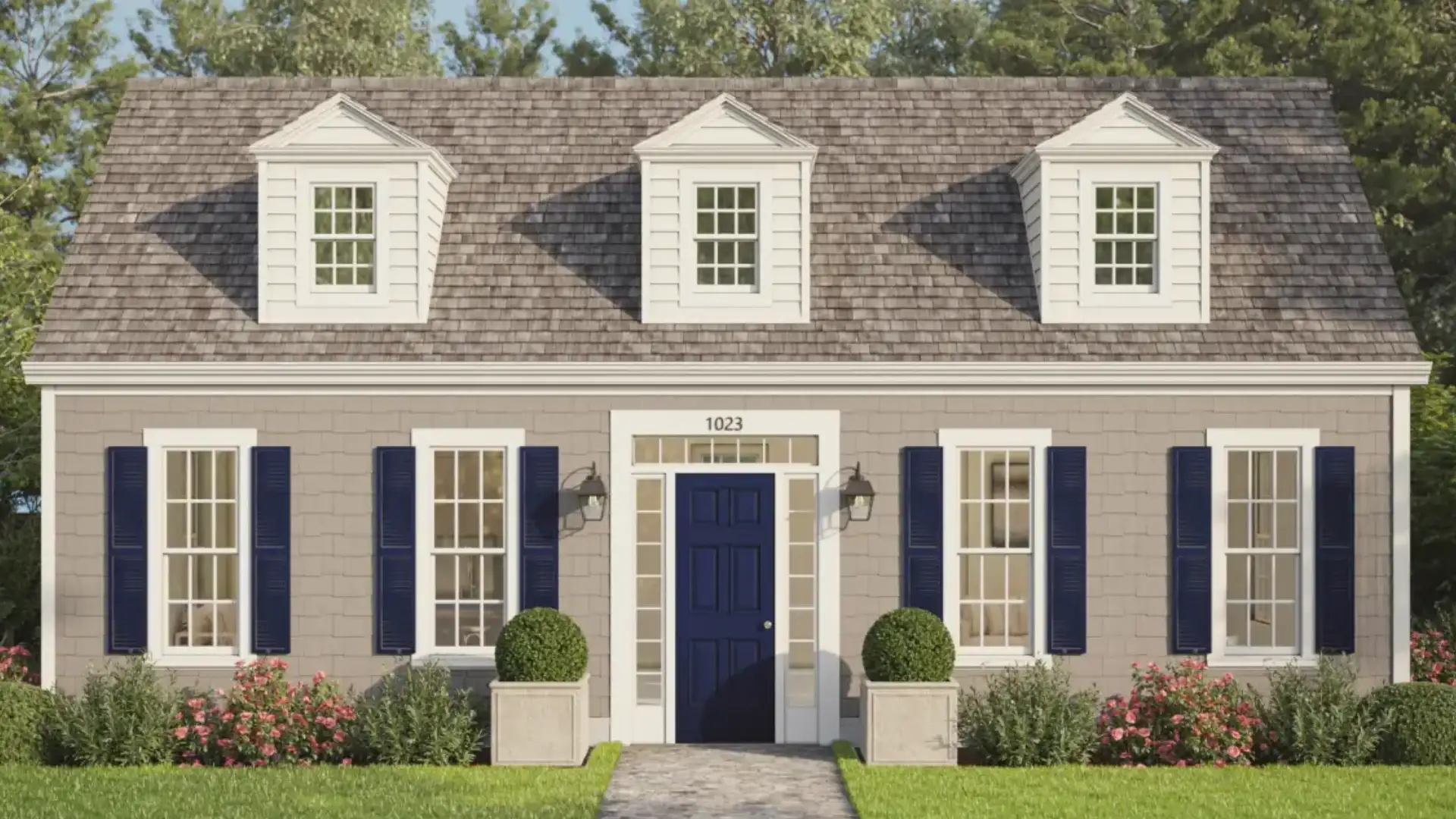 A tan-sided house with a dark blue door, white-trimmed windows with navy shutters, and three dormer windows under a gray shingled roof.