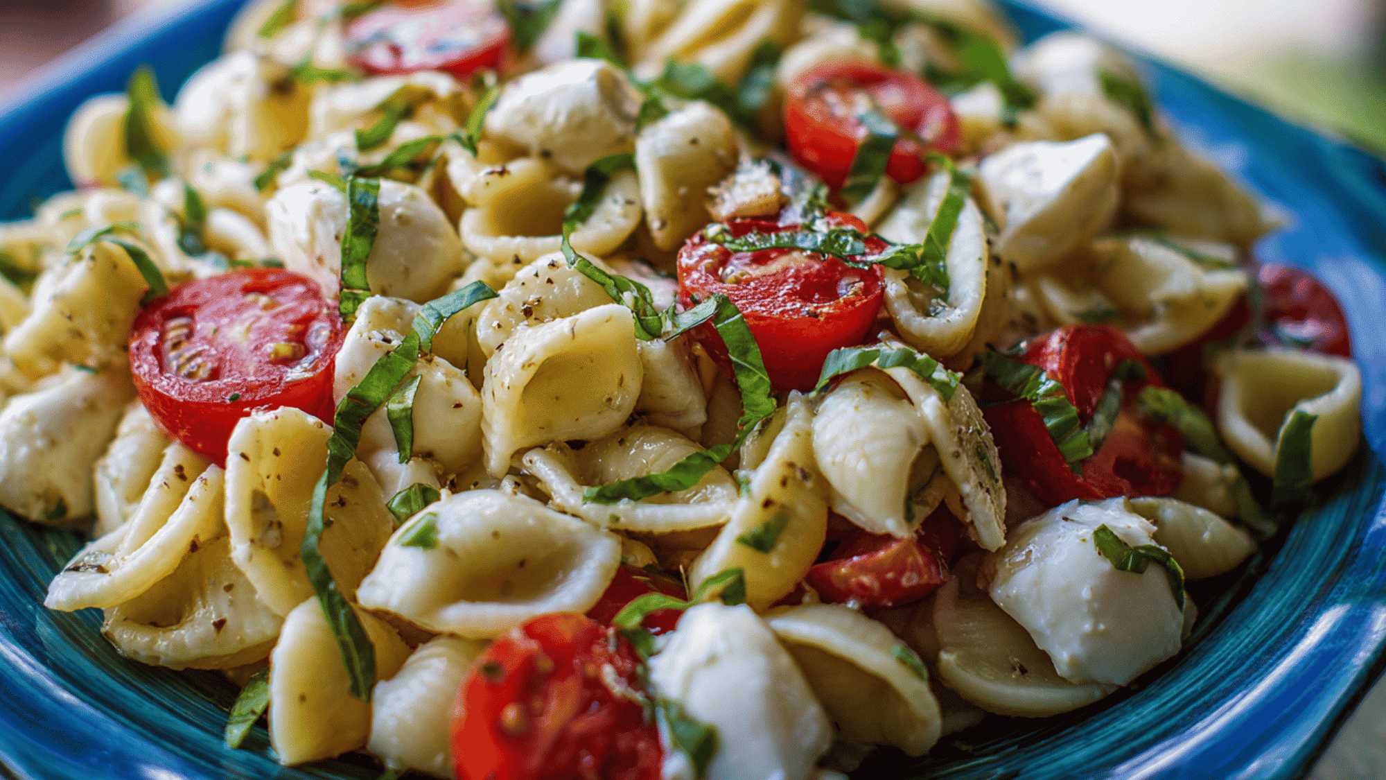A fresh caprese pasta salad with rotini, juicy cherry tomatoes, cubed mozzarella, and basil leaves in a meal prep container.