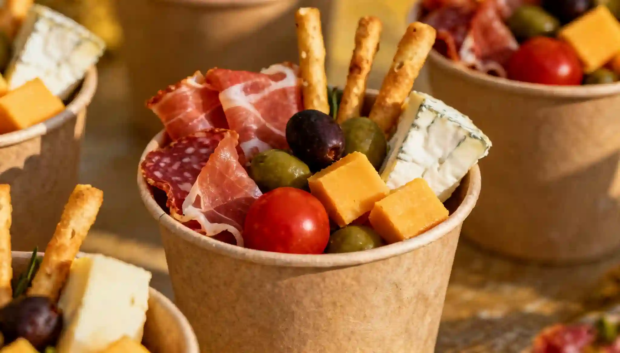 Individual charcuterie cups filled with cheese, cured meats, olives, cherry tomatoes, and breadsticks.
