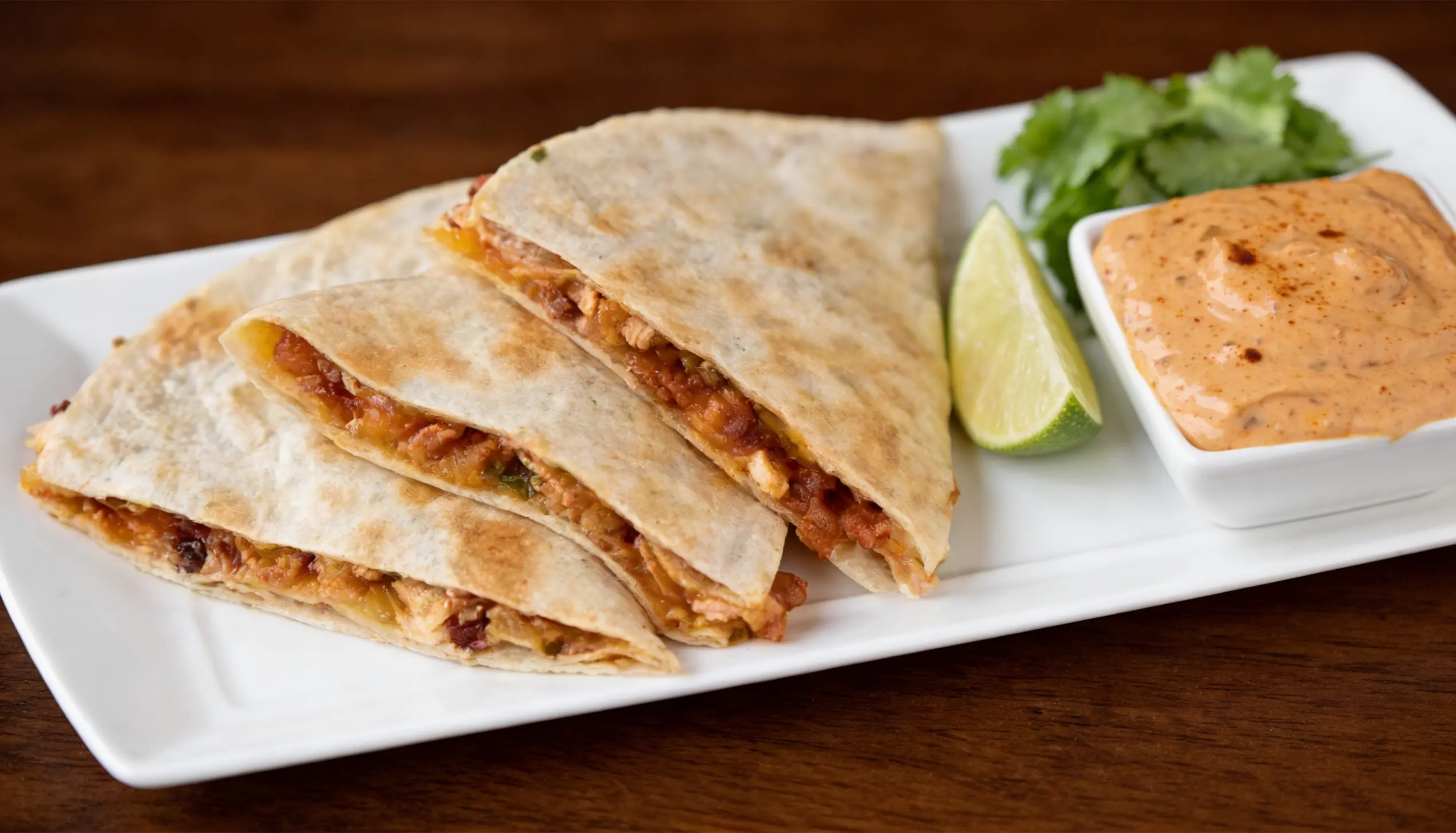 Chicken quesadillas with a side of spicy dipping sauce, lime wedges, and cilantro.