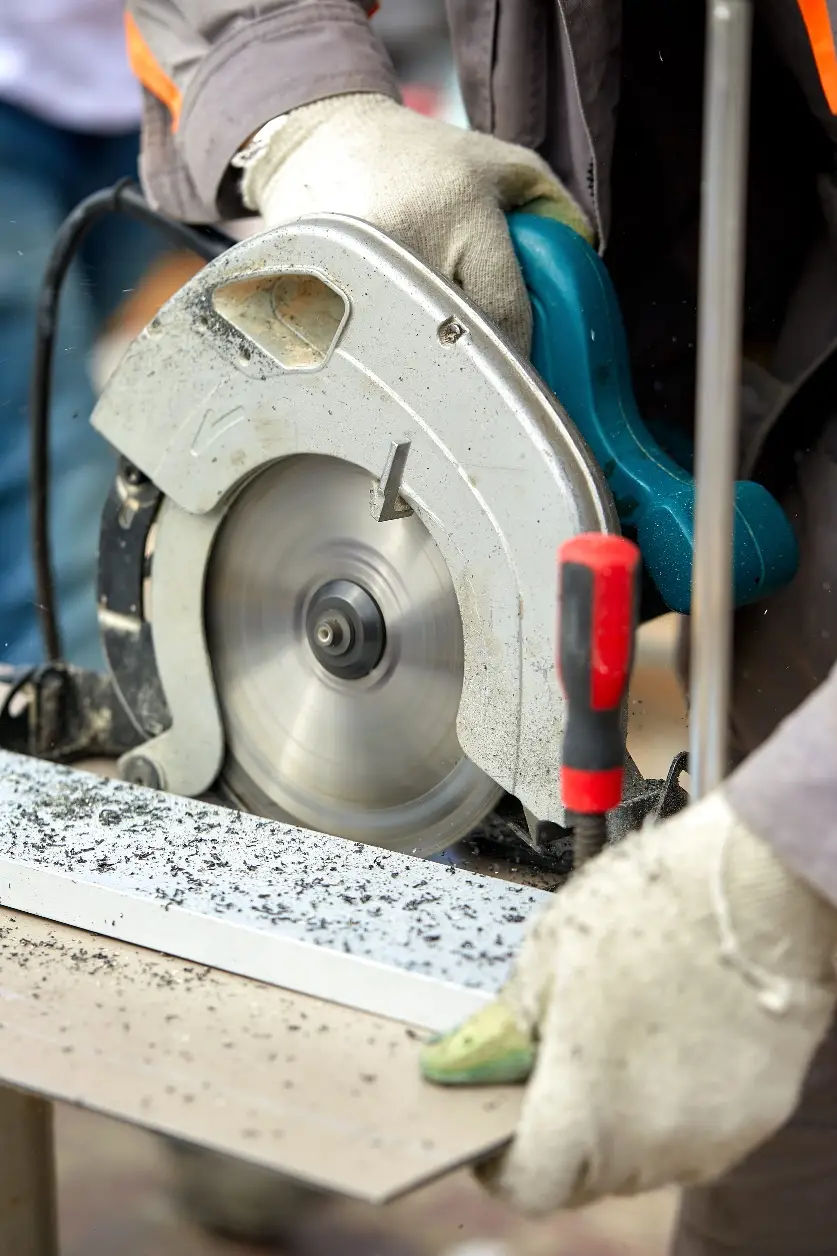 Worker cutting metal with circular saw in workshop, wearing protective gloves