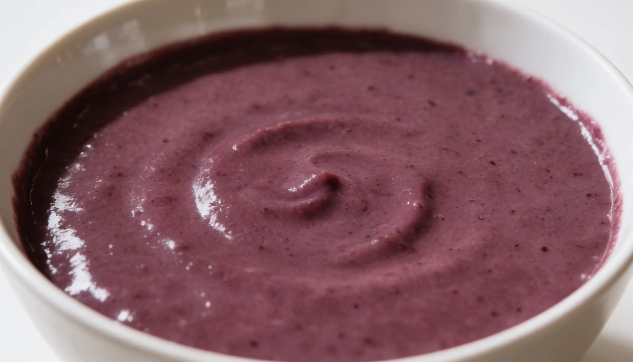 Close-up of purple blueberry smoothie swirled in a white bowl.