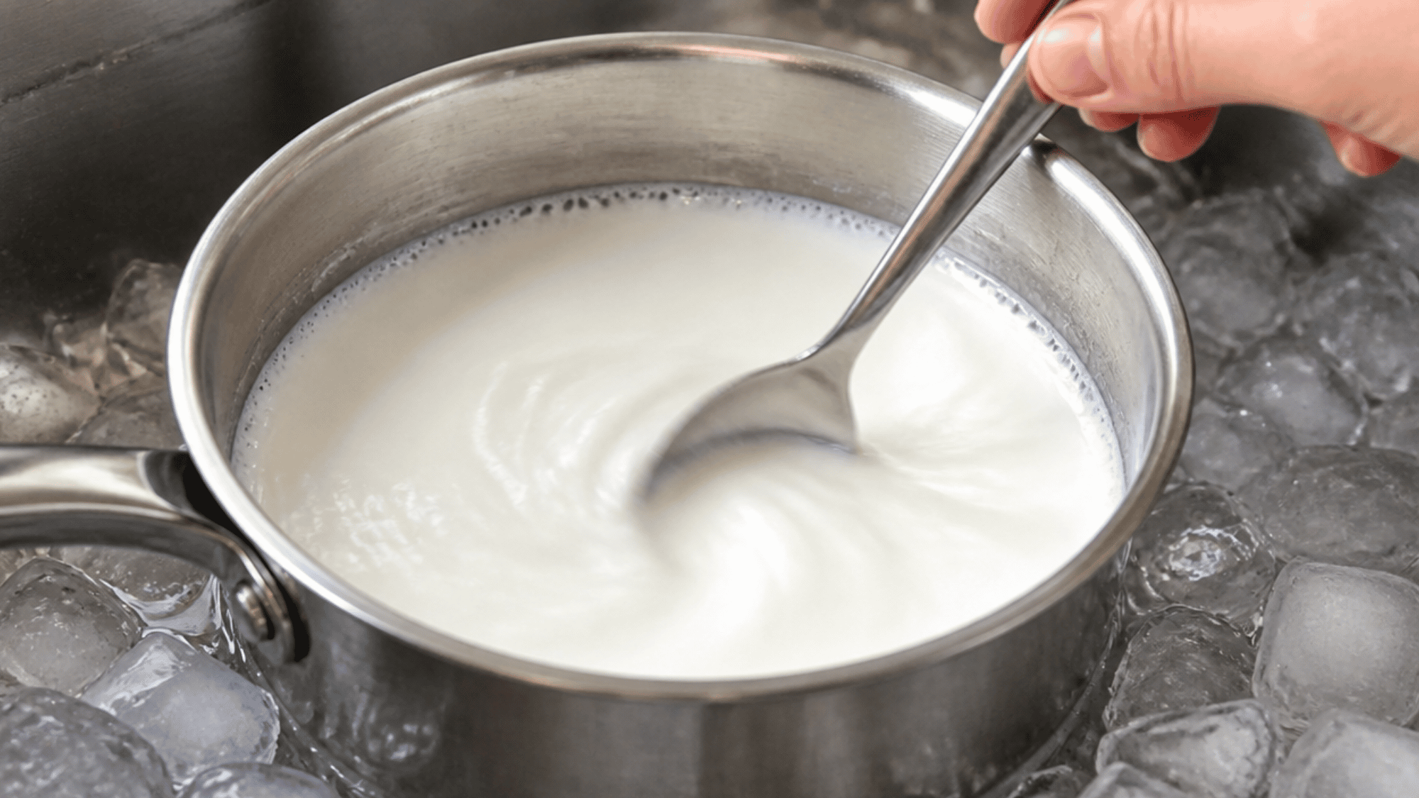 A saucepan filled with milk placed inside a sink filled with cold water to cool it down safely for yogurt making.