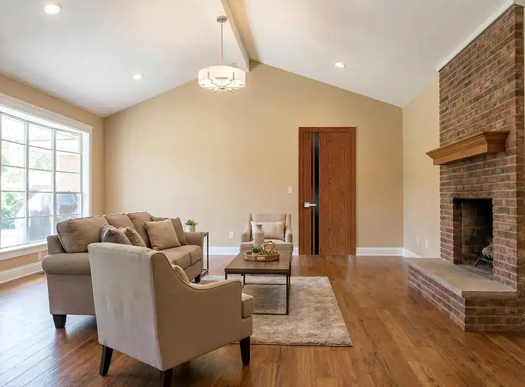 Neutral-toned living room with beige sofas, wooden floor, and brick fireplace under warm lighting