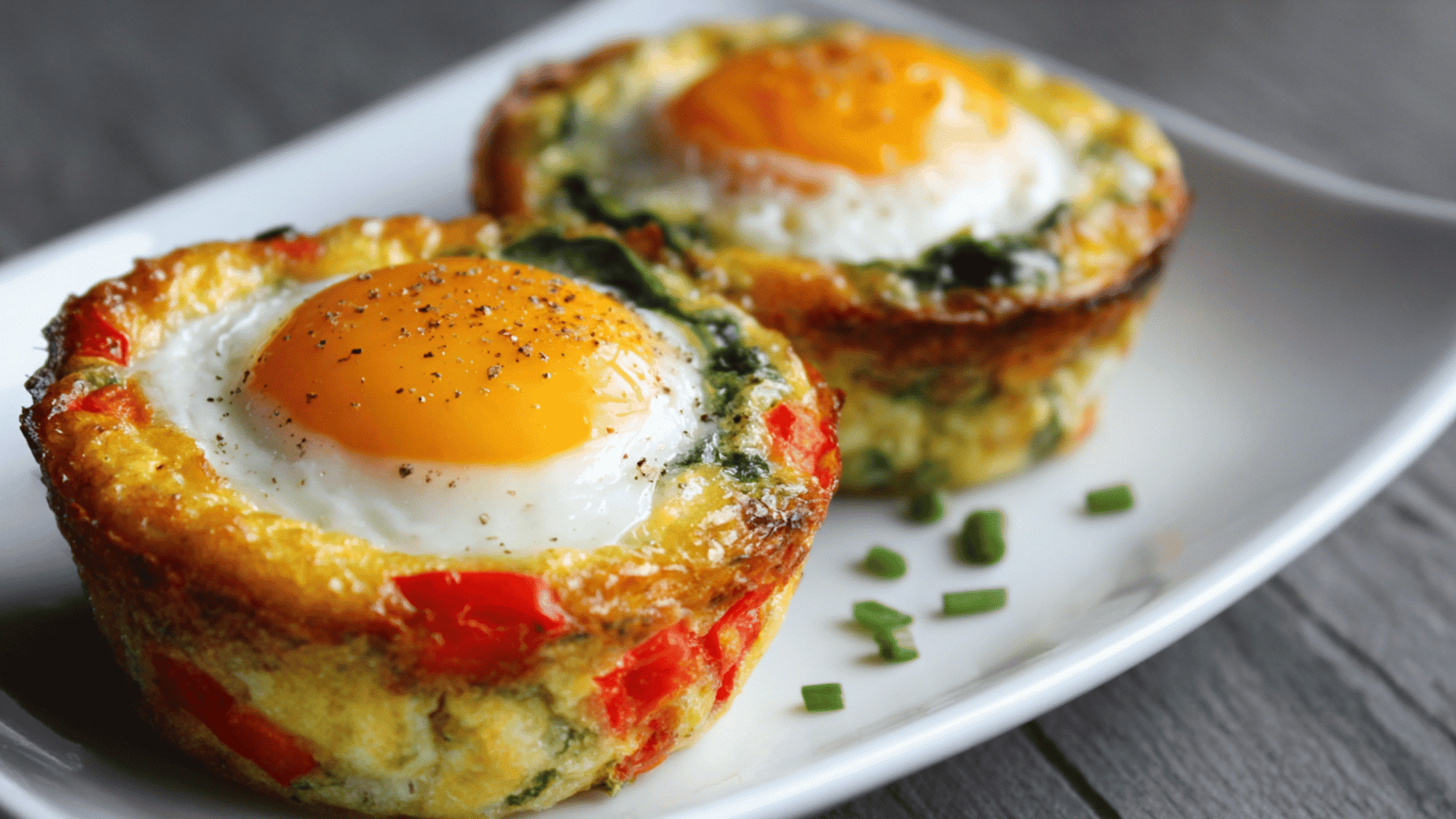Baked egg muffin cups packed with diced bell peppers, spinach, and melted cheese in a meal prep container.