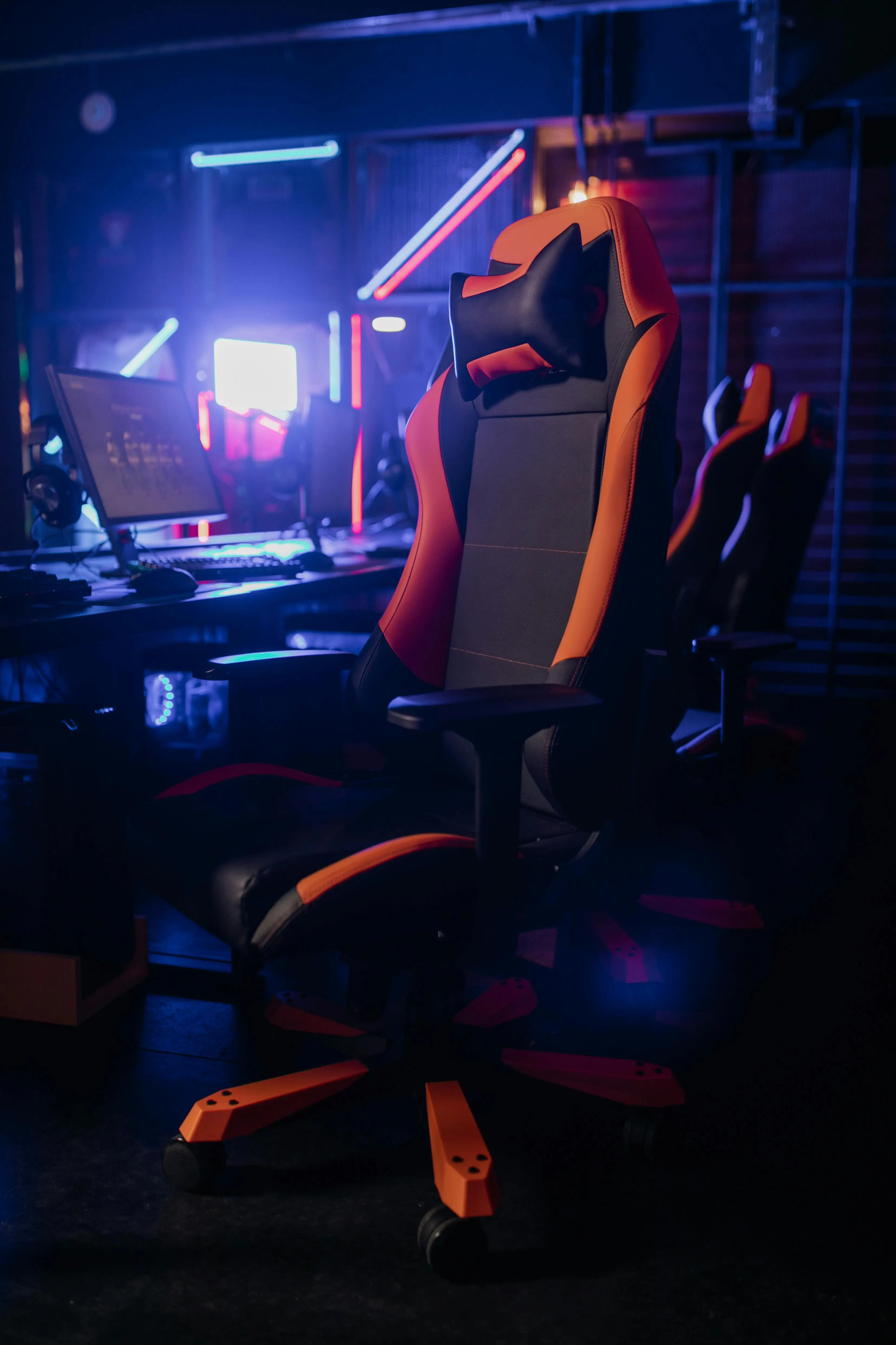 Gaming chair with orange and black design in dimly lit gaming setup with neon lights