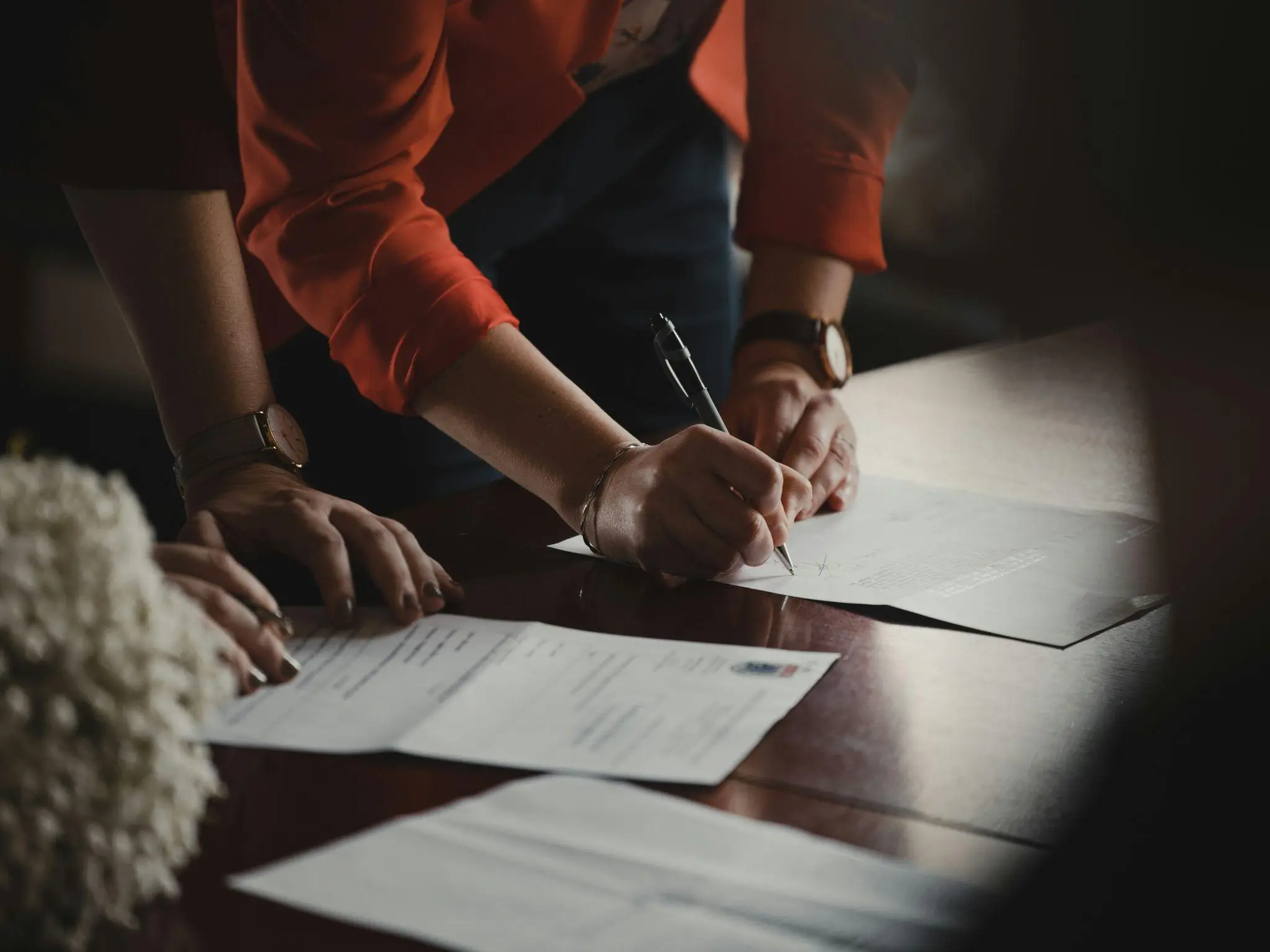 Person signing documents on wooden table with watch on wrist