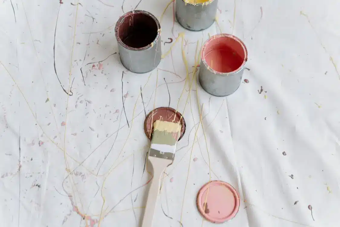 Open paint cans and brush on canvas with splattered paint drops