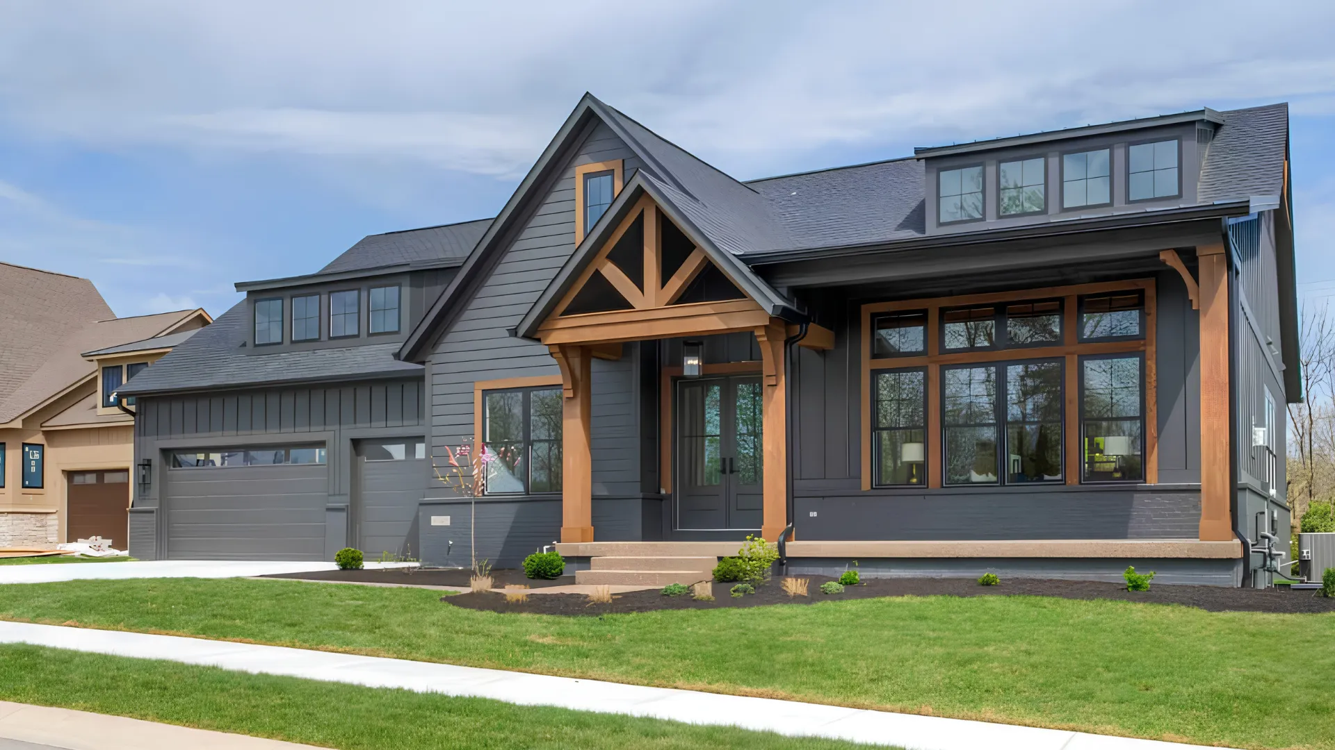 Modern dark gray house with wood accents, dormer windows, and a welcoming porch