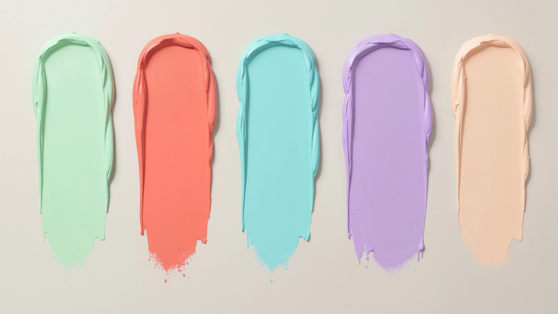 Swatches of green, coral, aqua, lavender, and peach concealer creams on a neutral background