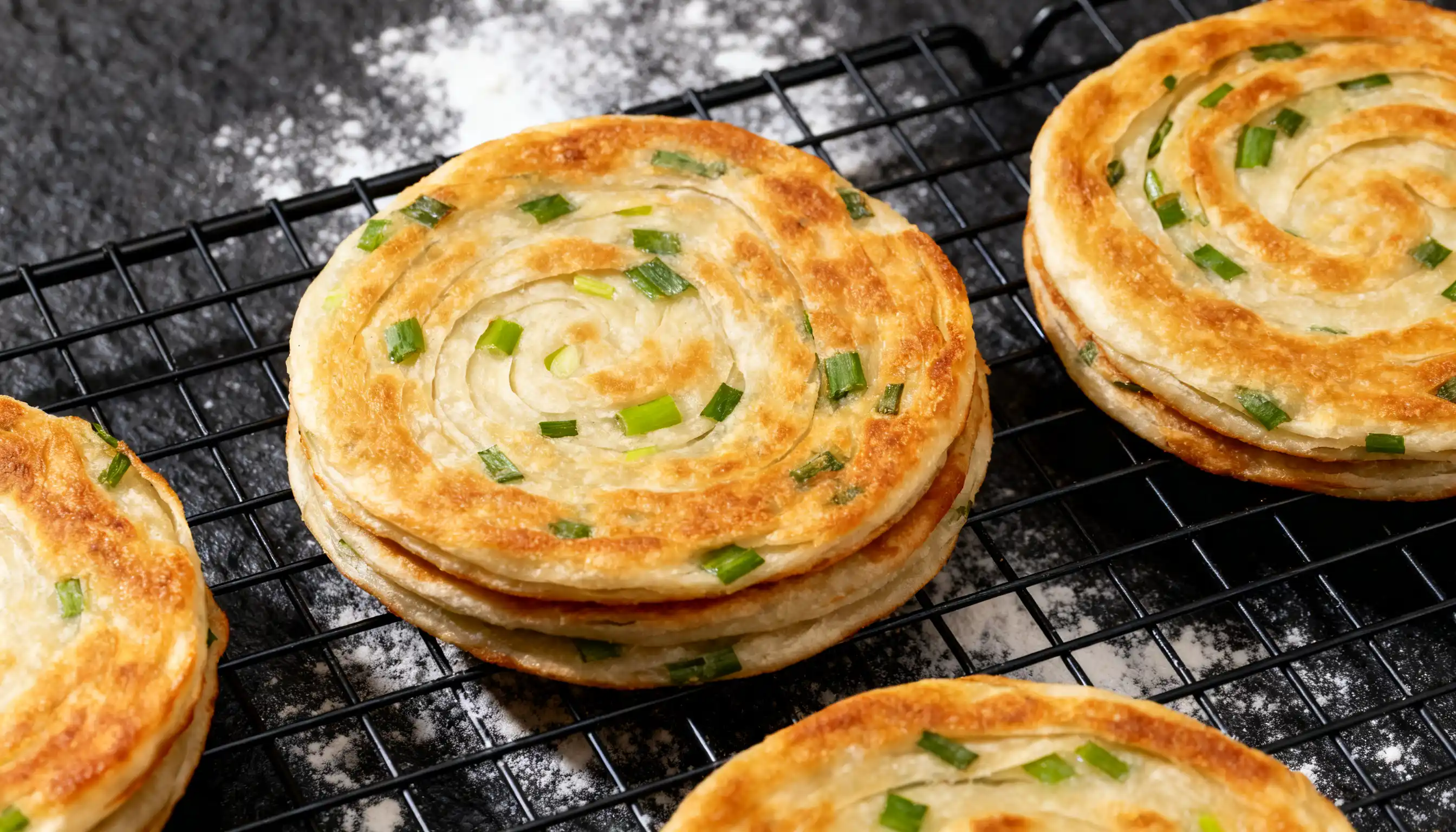 Deliciously golden and flaky <echighlighted><echighlighted><echighlighted><echighlighted>chinese scallion pancakes</echighlighted></echighlighted></echighlighted></echighlighted> stacked on a cooling rack, showcasing their spiral layers and fresh ingredients.