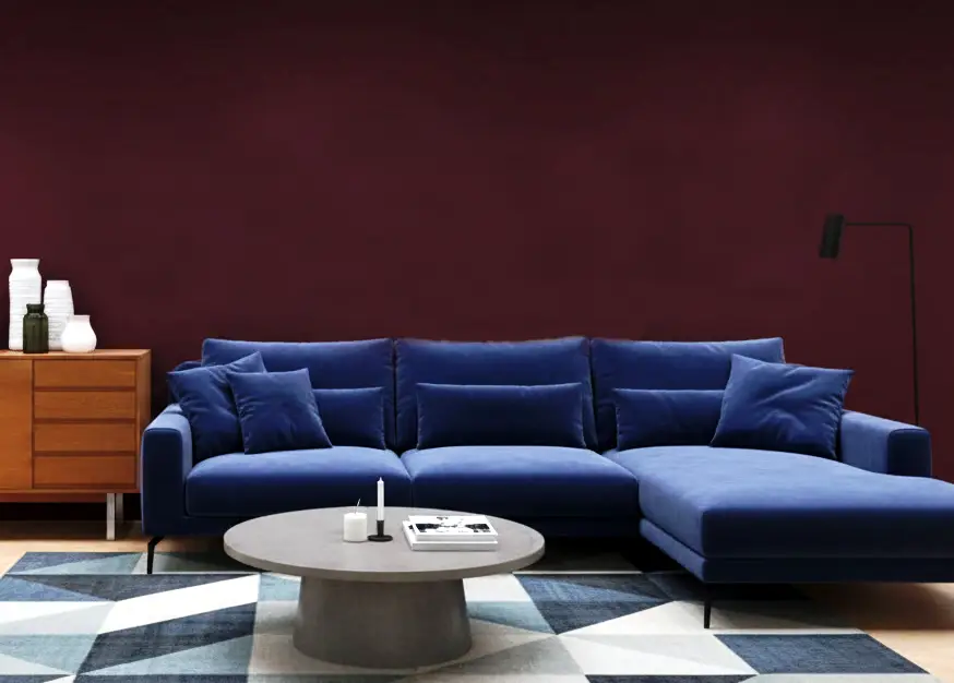 Blue sectional sofa in modern living room with burgundy wall and geometric rug