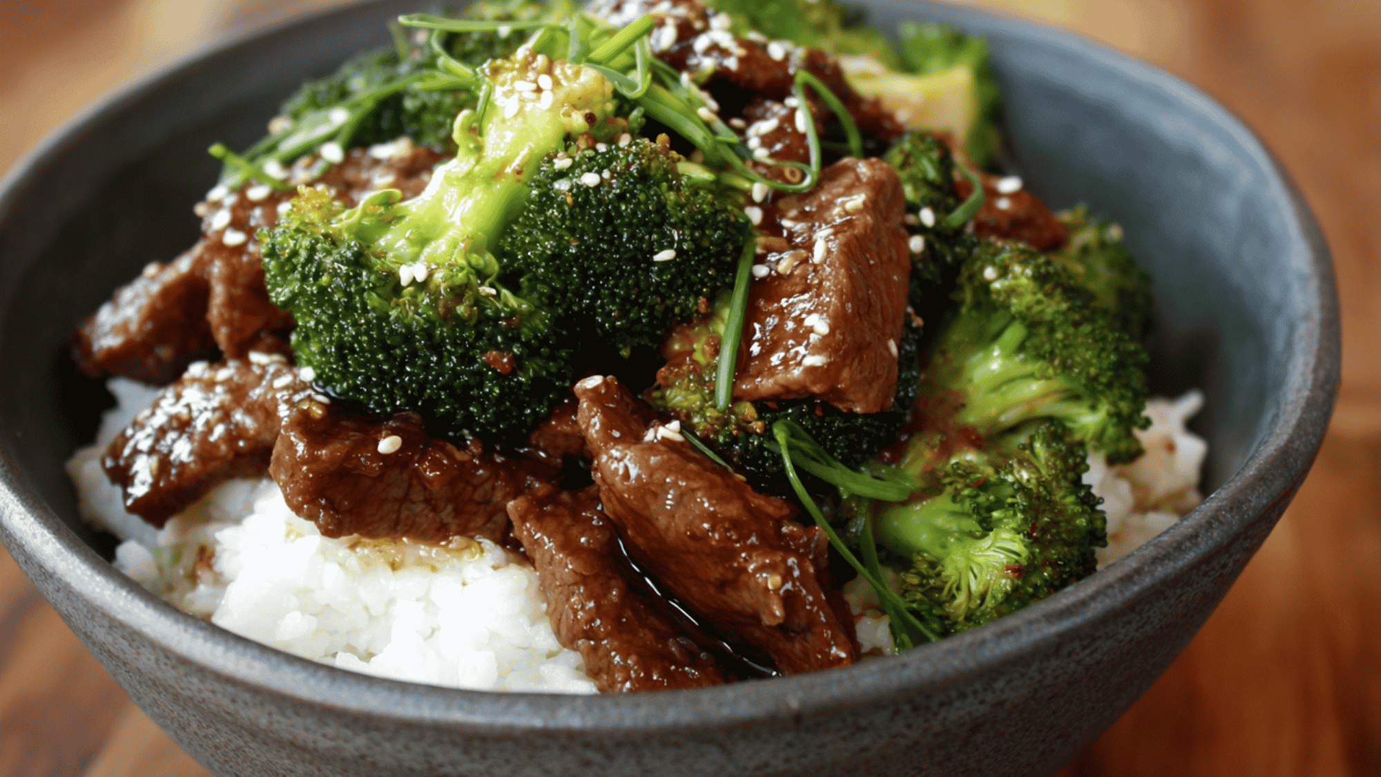 A savory meal prep bowl featuring thinly sliced, seared lean sirloin beef and vibrant green broccoli florets tossed in a glossy soy-ginger sauce, served over a bed of fluffy brown rice.