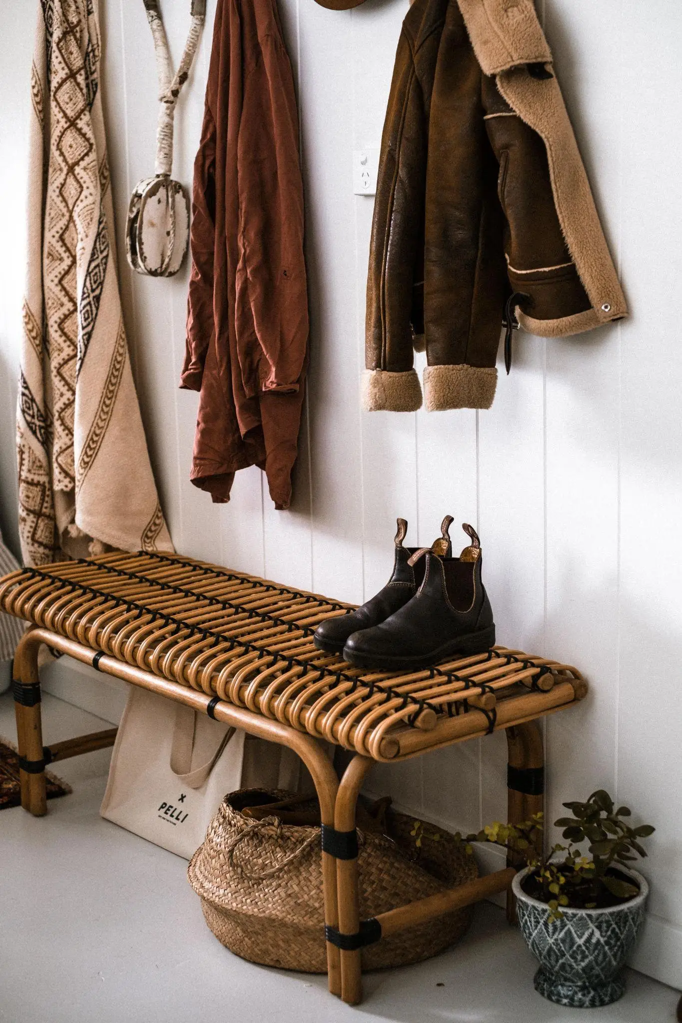 Wicker bench with black boots and hanging coats in cozy entryway
