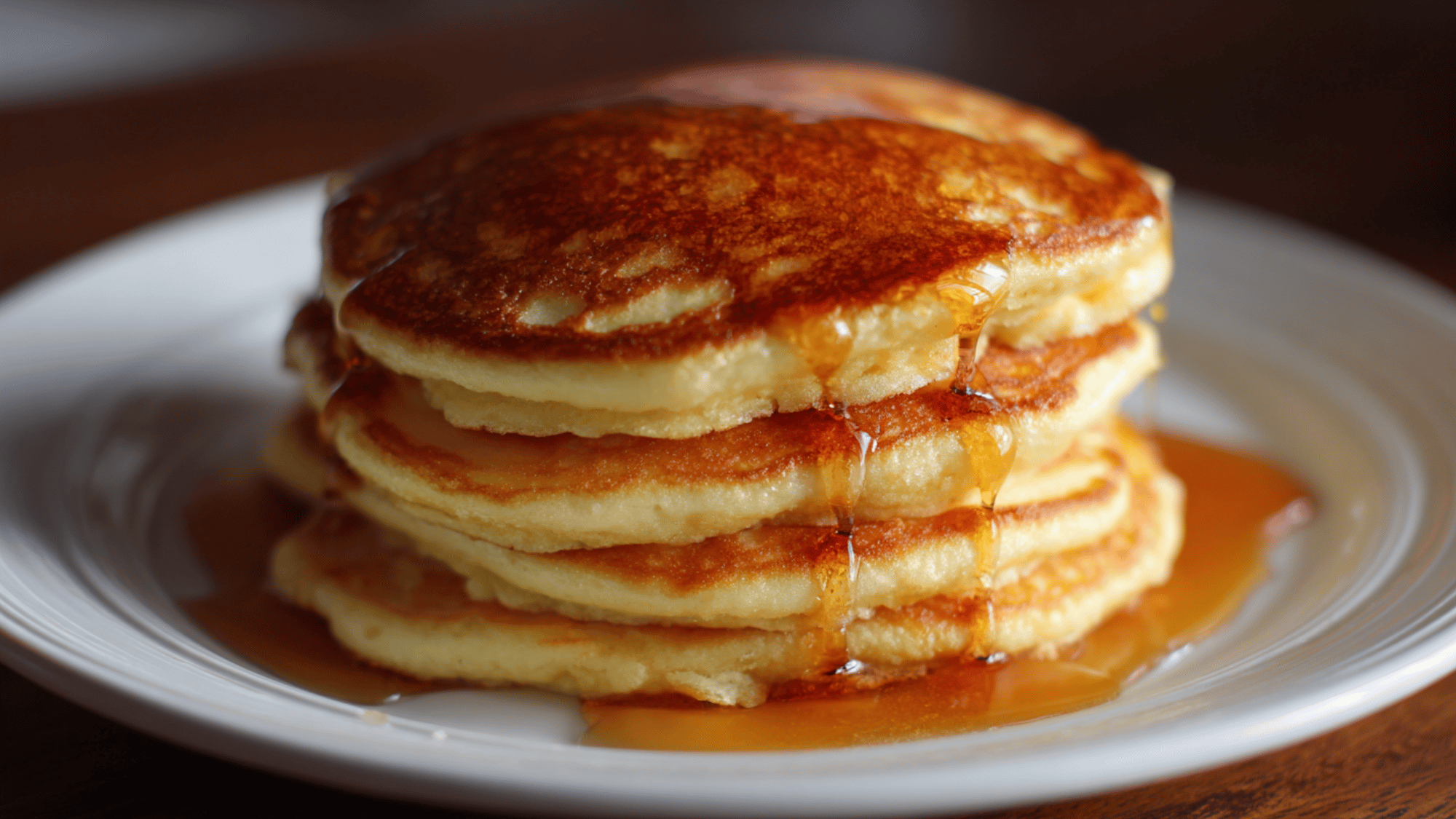 A tall stack of fluffy, golden pancakes topped with butter and maple syrup.