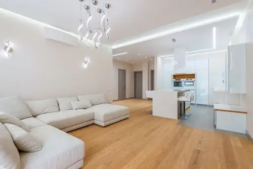 Spacious modern living room with beige sectional sofa and wooden flooring under sleek lighting fixtures