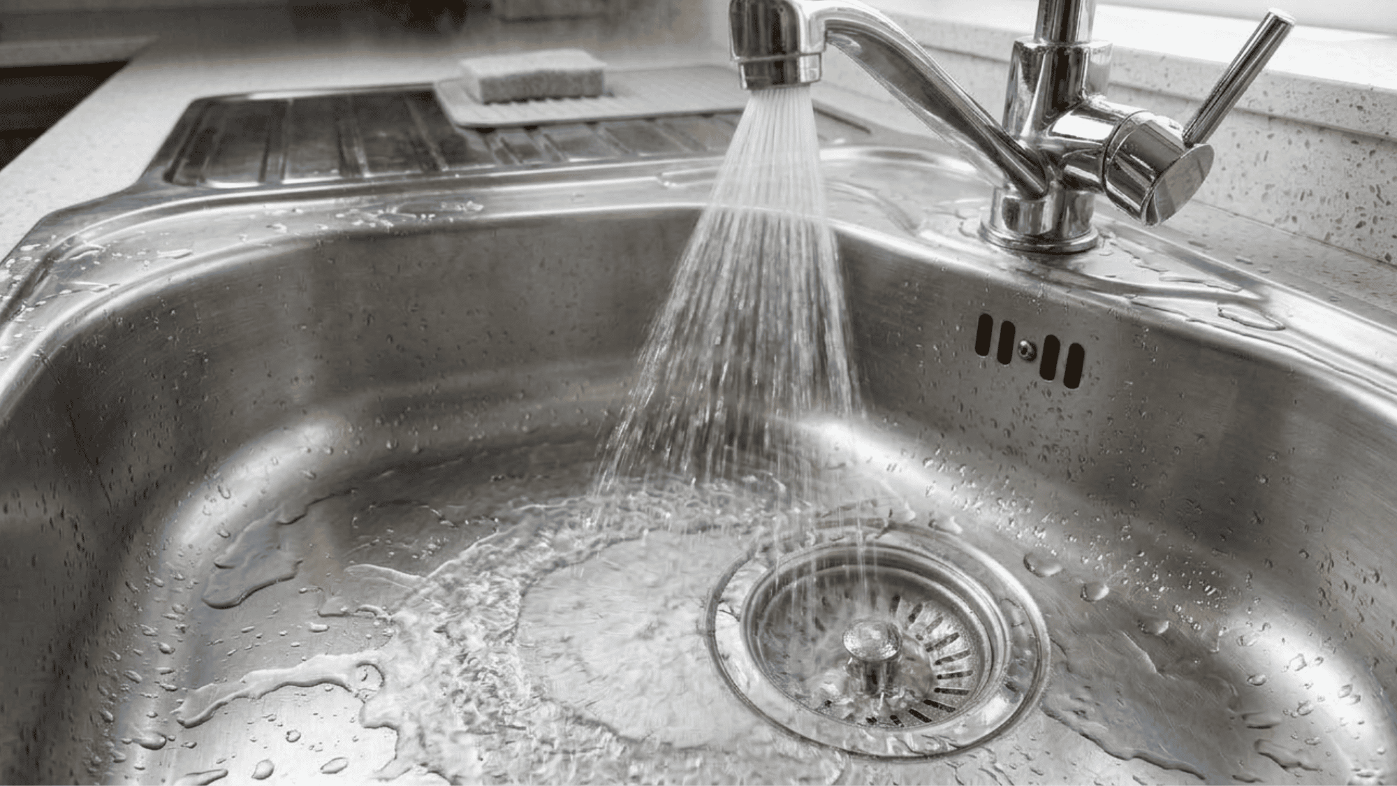 Warm water rinsing away the baking soda and vinegar mixture from a clean, shiny stainless steel sink basin.