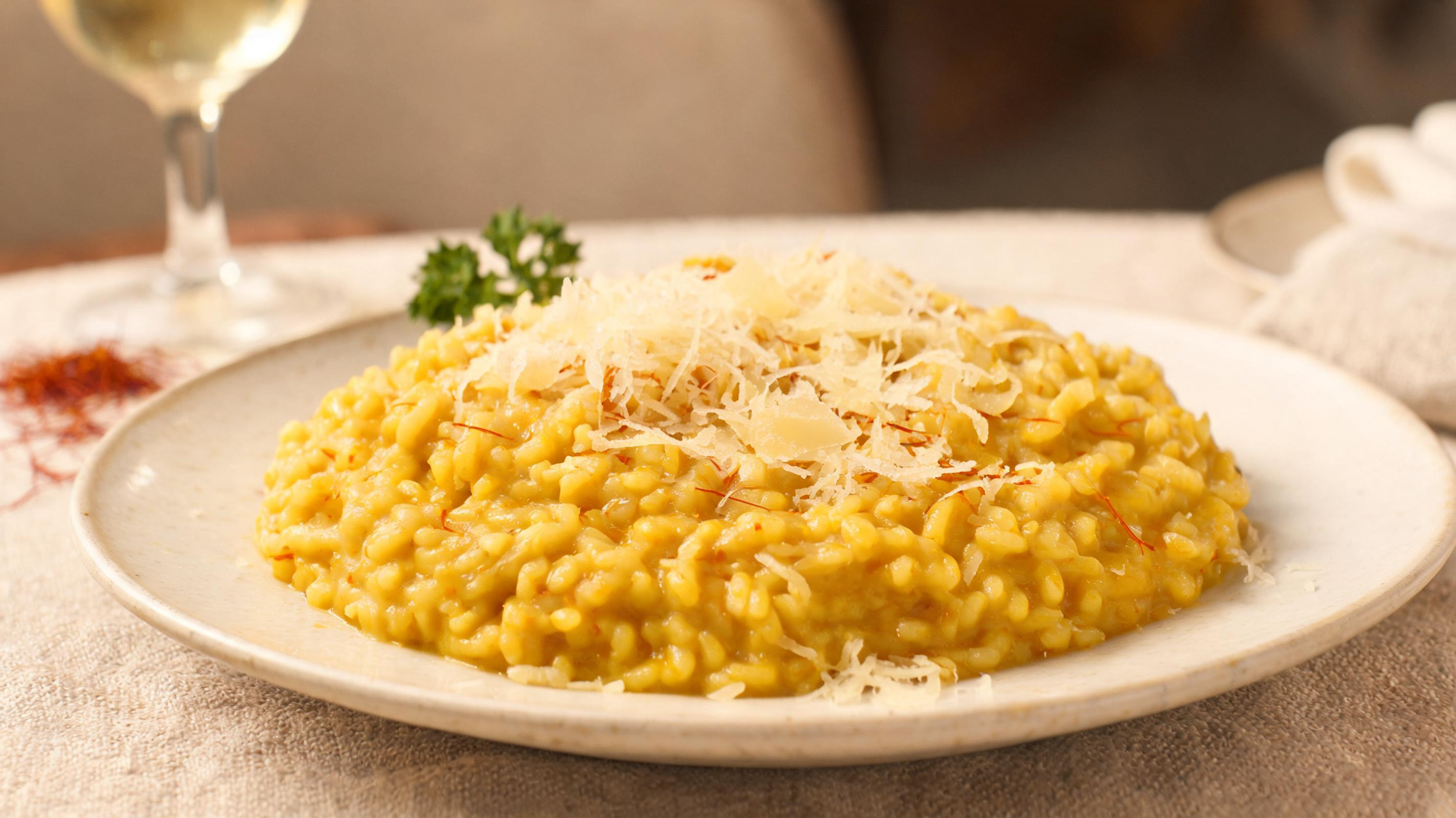 Plate of golden Risotto alla Milanese topped with shaved Parmigiano, cozy kitchen setting.