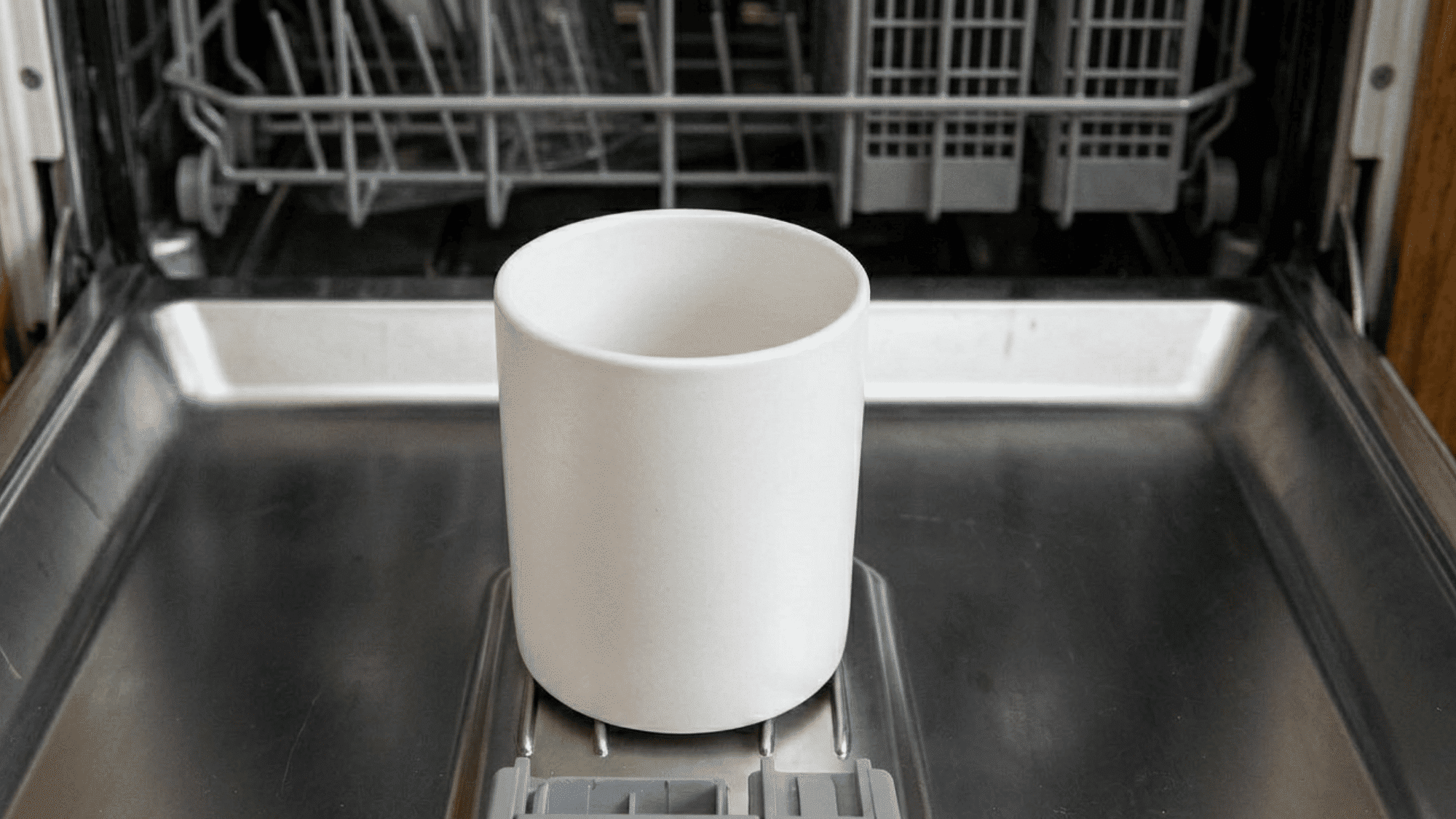 White cup placed in dishwasher rack during hot cleaning cycle inside kitchen appliance now