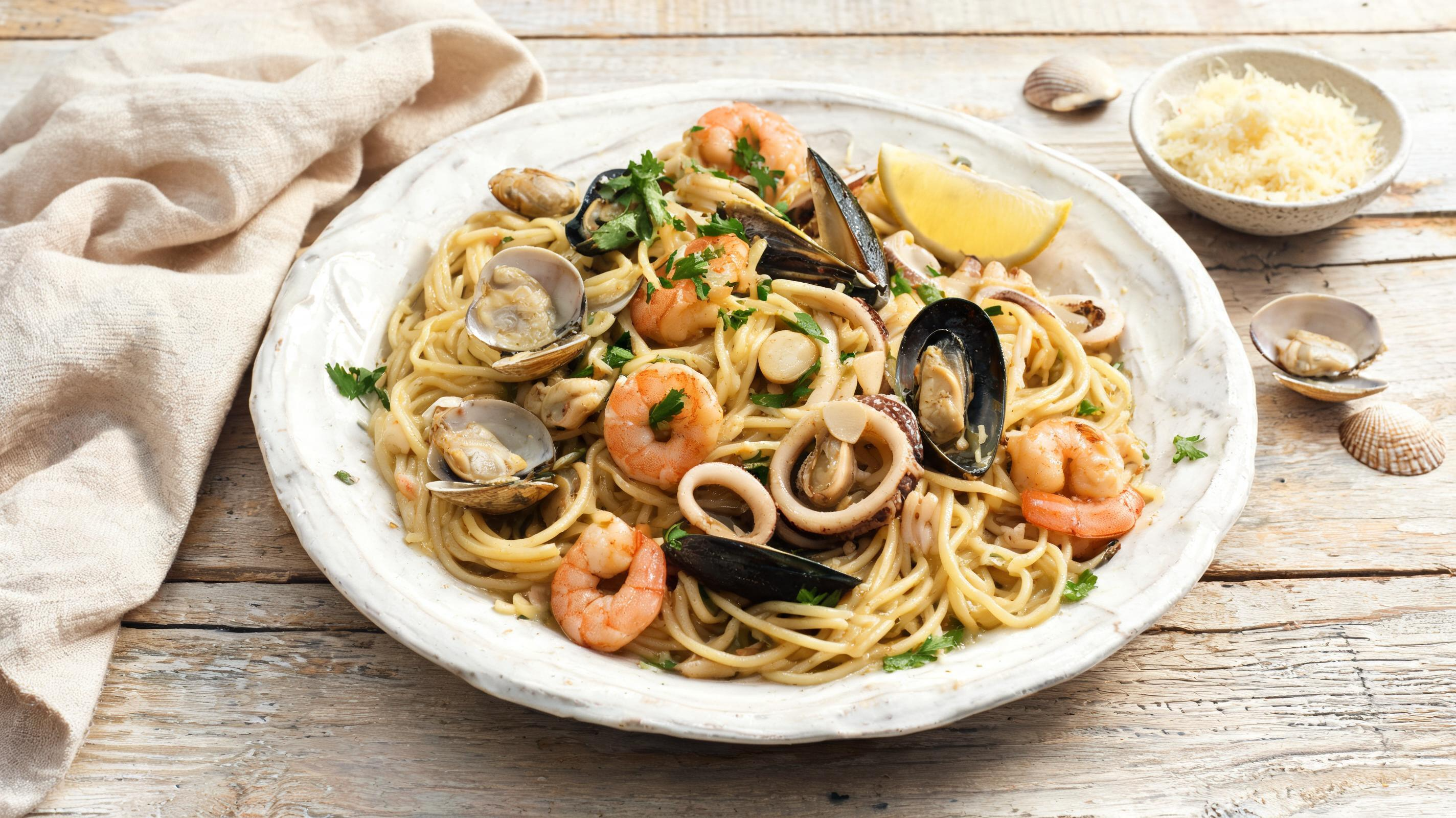 Golden-brown seafood pasta with shrimp, mussels, clams, parsley, and lemon wedges.
