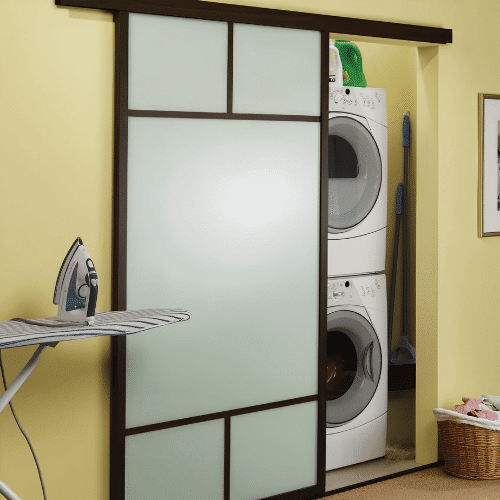 > Stacked washer and dryer closet hidden behind a frosted glass sliding barn door with yellow walls