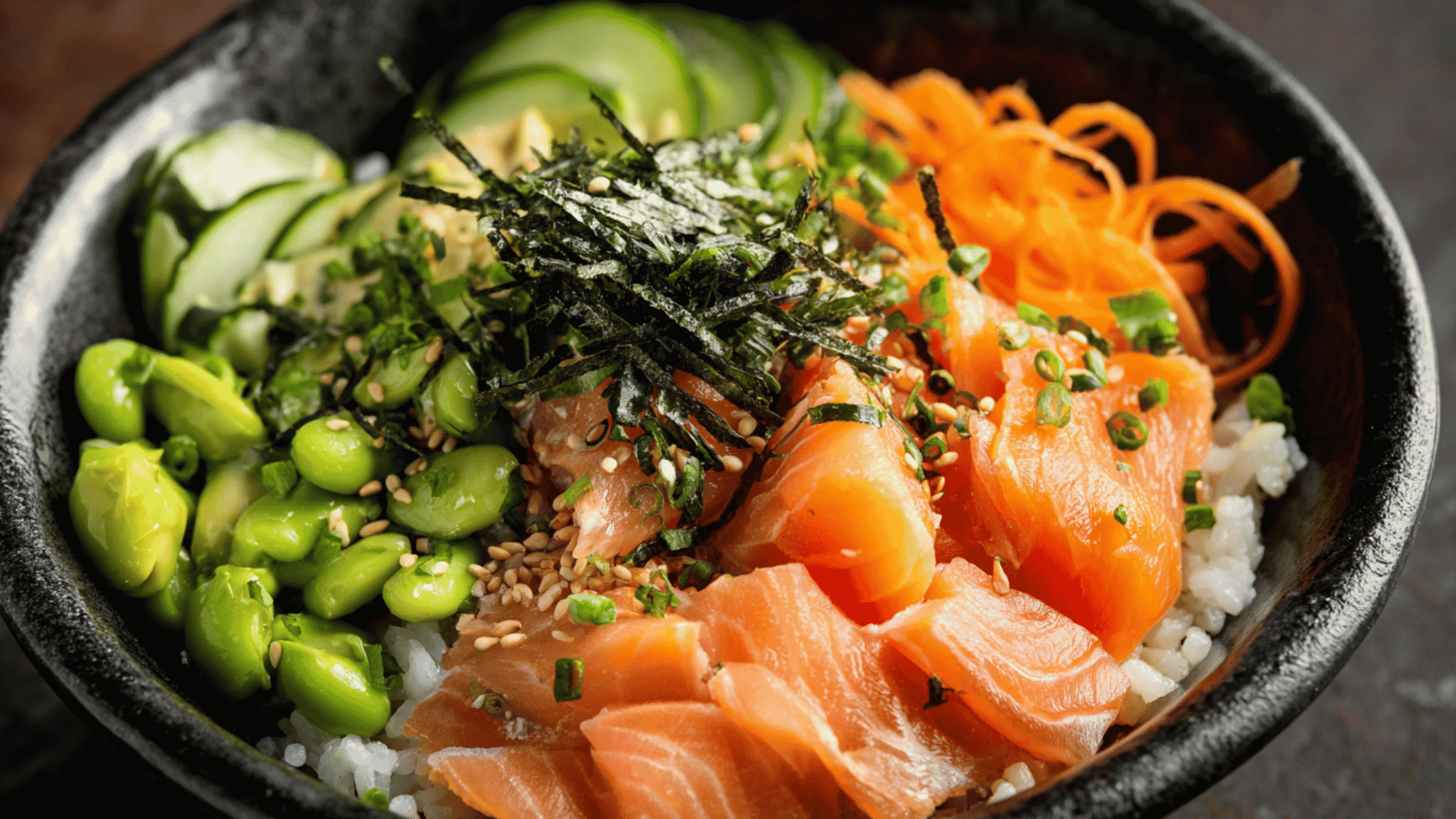 A fresh smoked salmon rice bowl featuring sliced smoked salmon, shredded carrots, thinly sliced cucumber, pickled red onion, and sliced avocado arranged over a bed of brown rice.