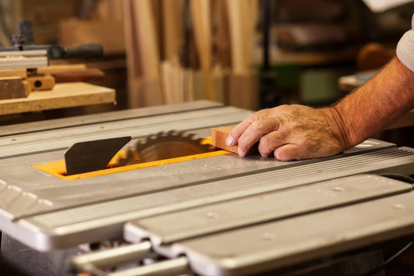 Hand guiding wood along table saw in a woodworking workshop