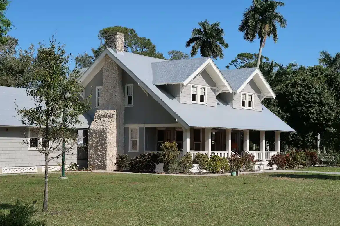 Gray Craftsman-style house with stone chimney and front porch in sunny garden setting
