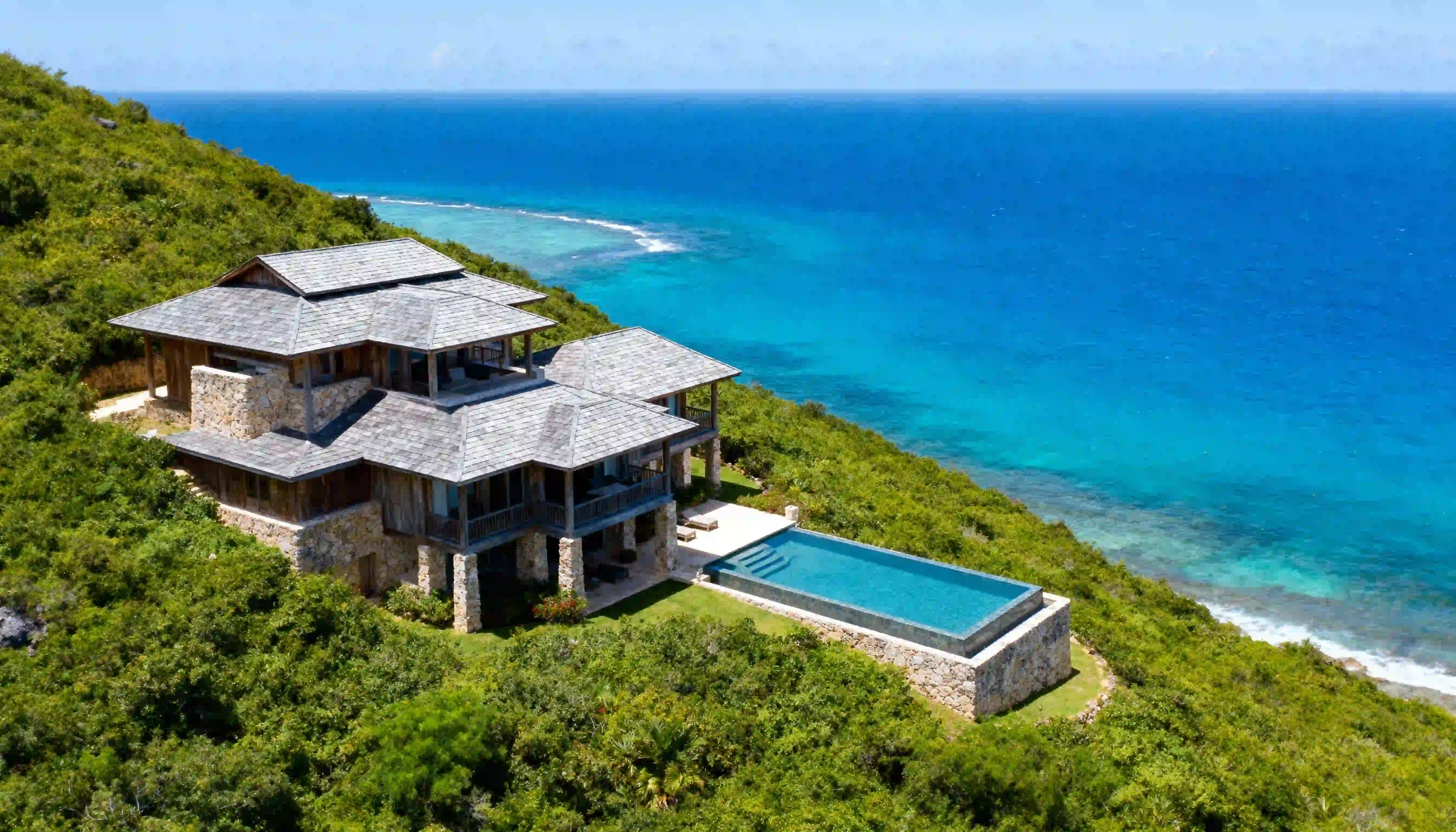 aerial view of a tropical stone villa with louvered windows infinity pool and ocean views on a hillside