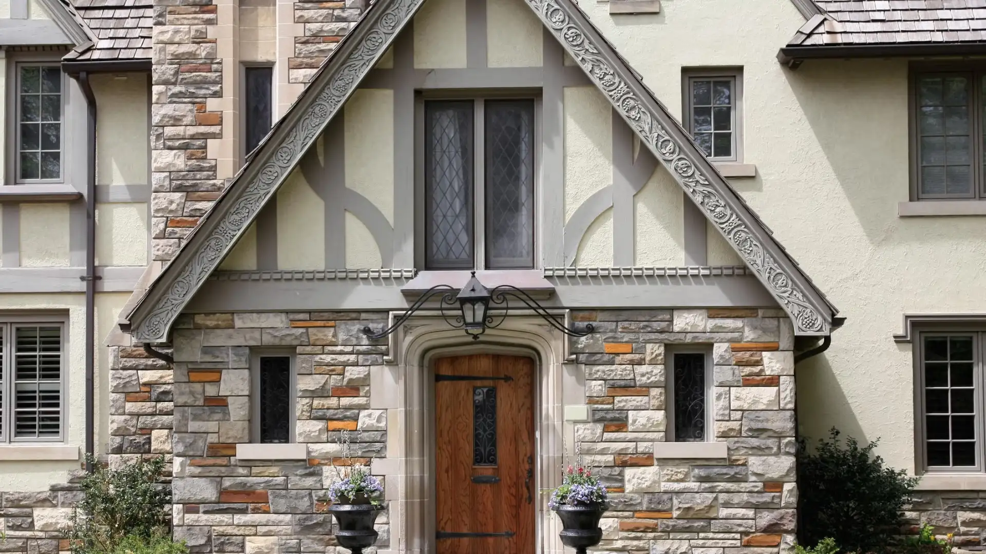 Close-up of an ornate stone-clad Tudor-style home entrance with a wooden door and decorative window.
