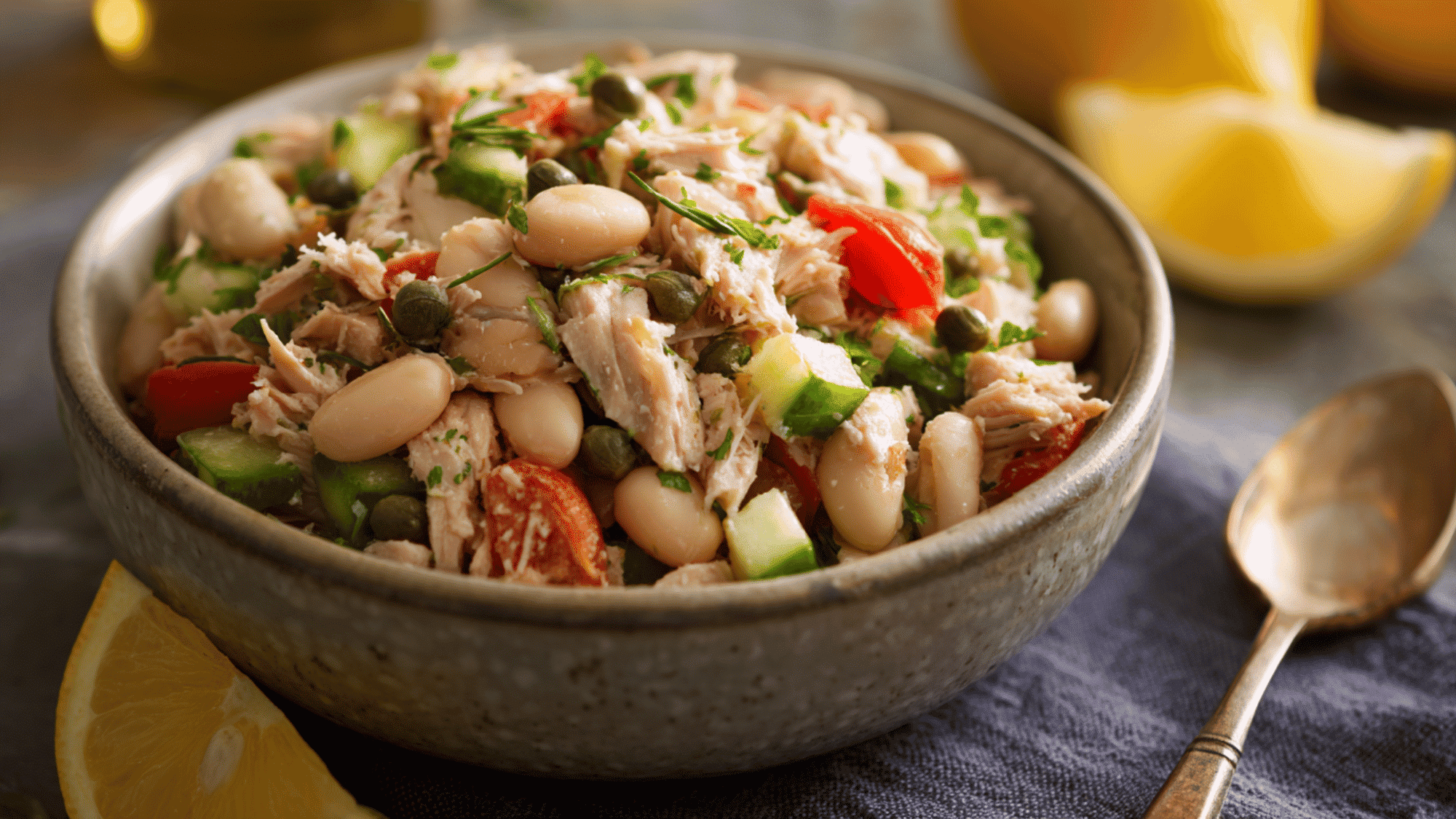 Protein-rich tuna and cannellini bean salad in a meal prep container, mixed with capers, red onion, and fresh arugula.