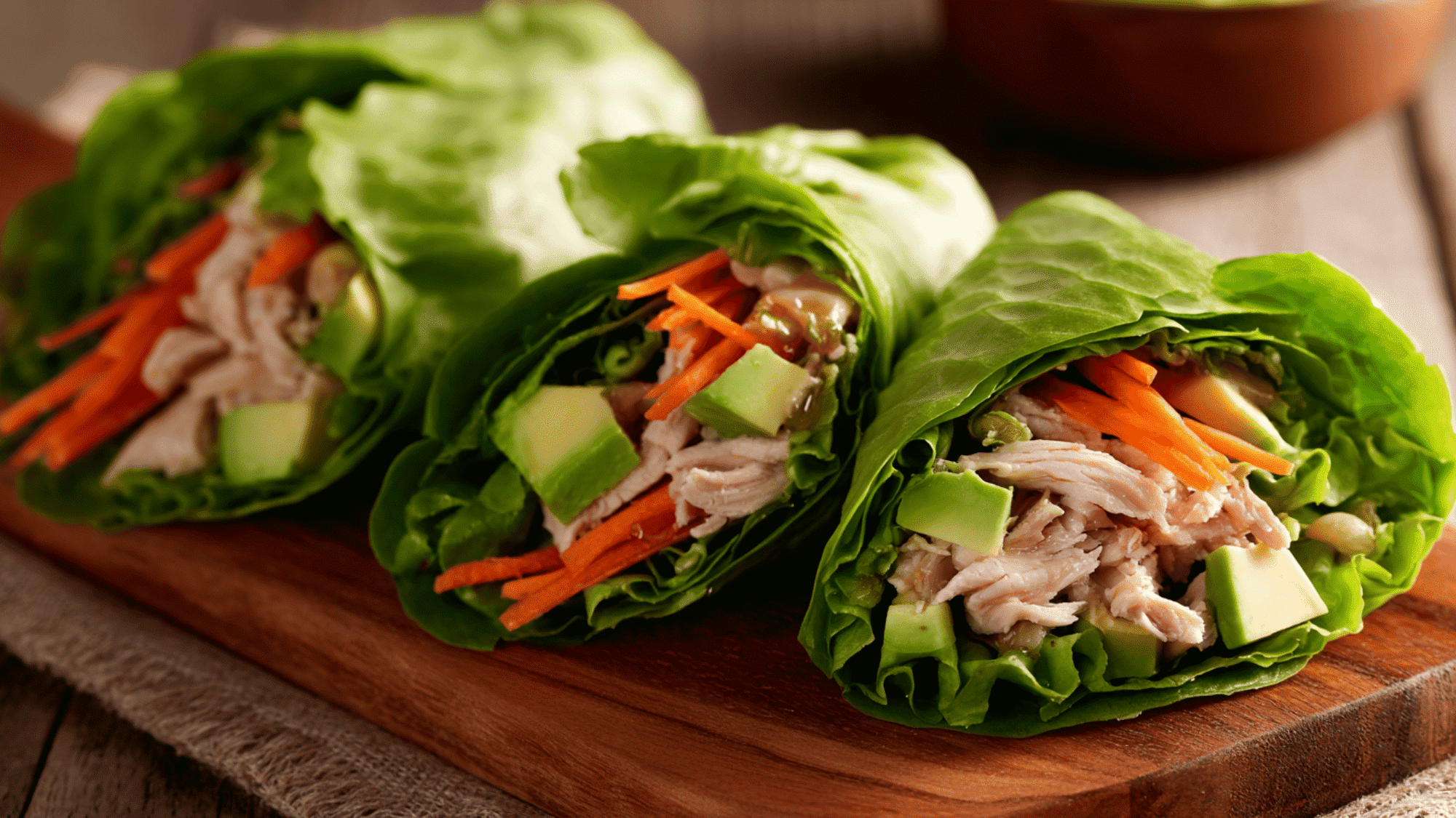 Turkey and avocado lettuce wraps in a meal prep container with shredded carrots and a side of hummus.