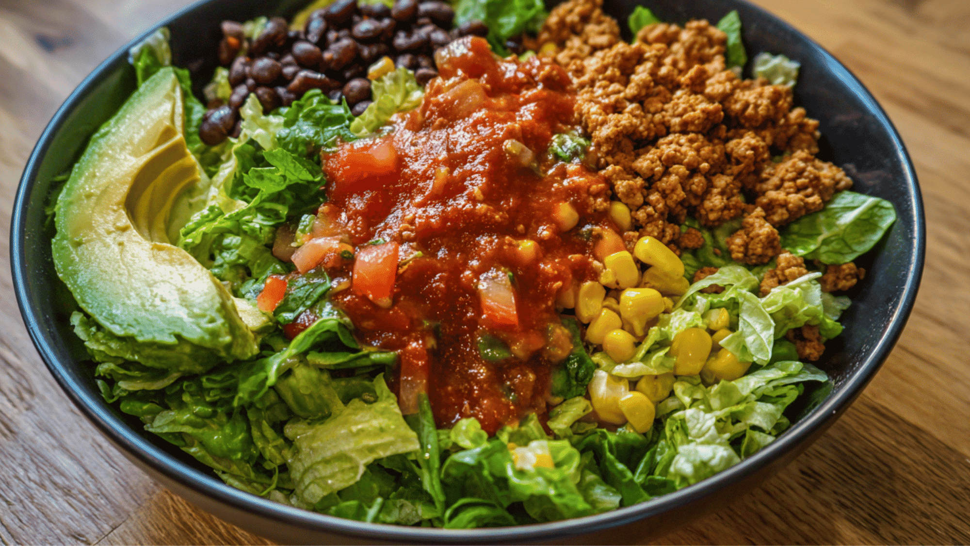 A flavorful turkey taco salad bowl in a meal prep container, featuring a base of crisp romaine lettuce layered with seasoned ground turkey, black beans, sweet corn, and a fresh scoop of pico de gallo.