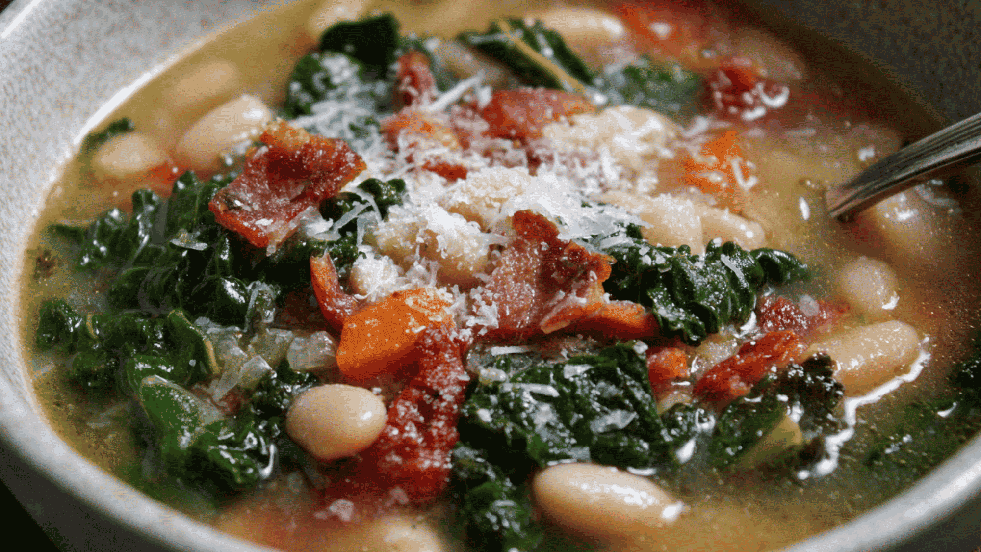 A nourishing bowl of white bean and kale soup in a meal prep container, seasoned with fresh rosemary and red pepper flakes.