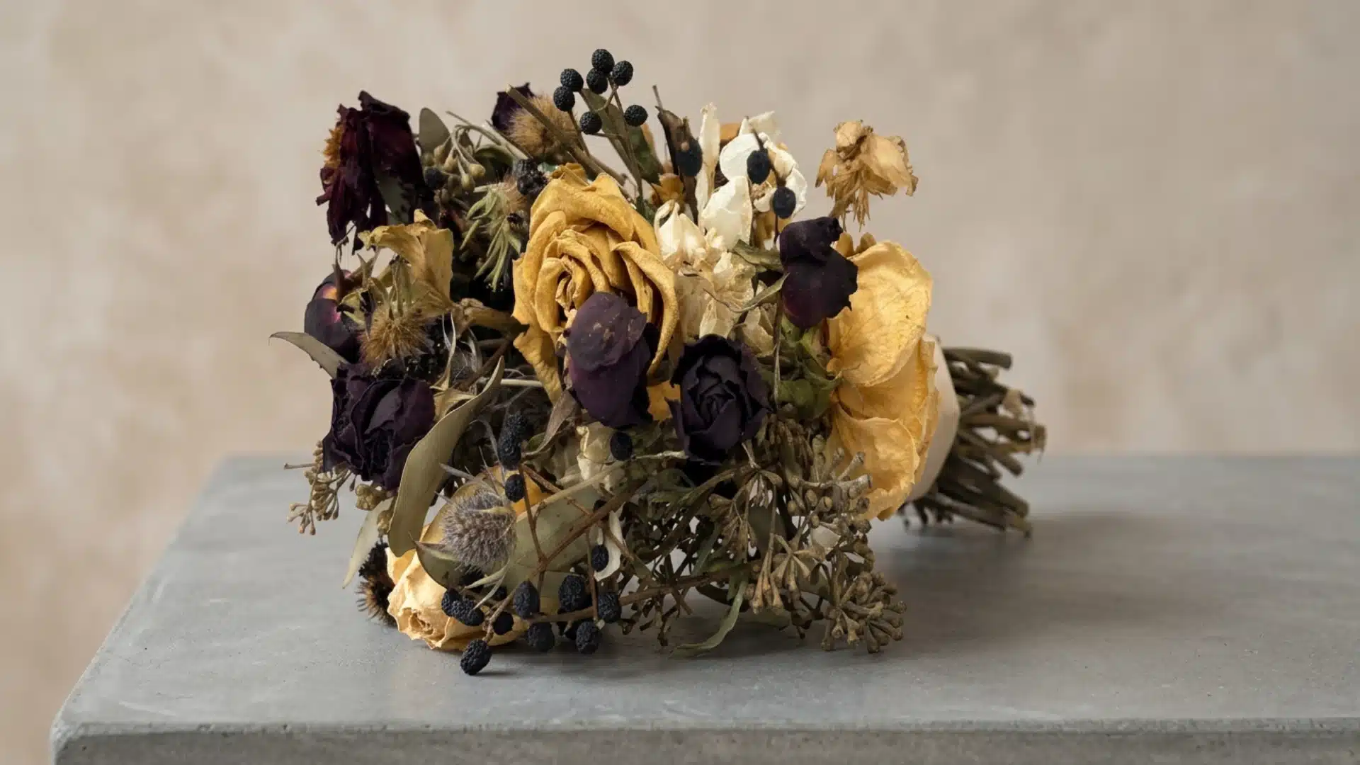 Air-dried bouquet with yellow and dark purple flowers resting on a gray surface.