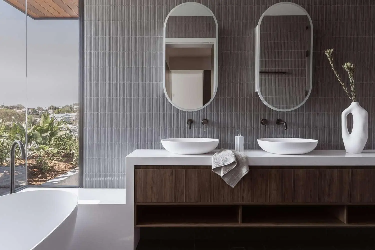 Modern bathroom with double sink vanity, oval mirrors, and a vase on gray tiled wall