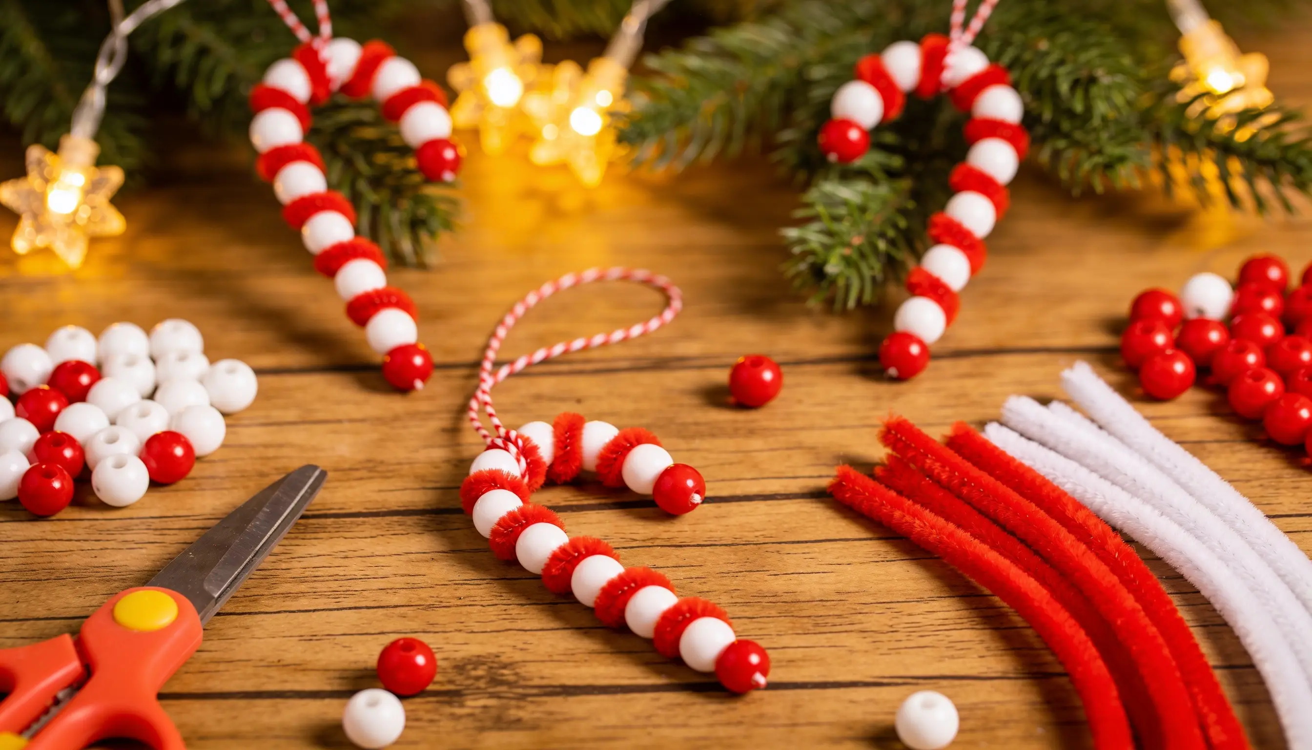 Christmas craft supplies including handmade candy cane ornaments, beads, pipe cleaners, and scissors are arranged on a wooden surface.
