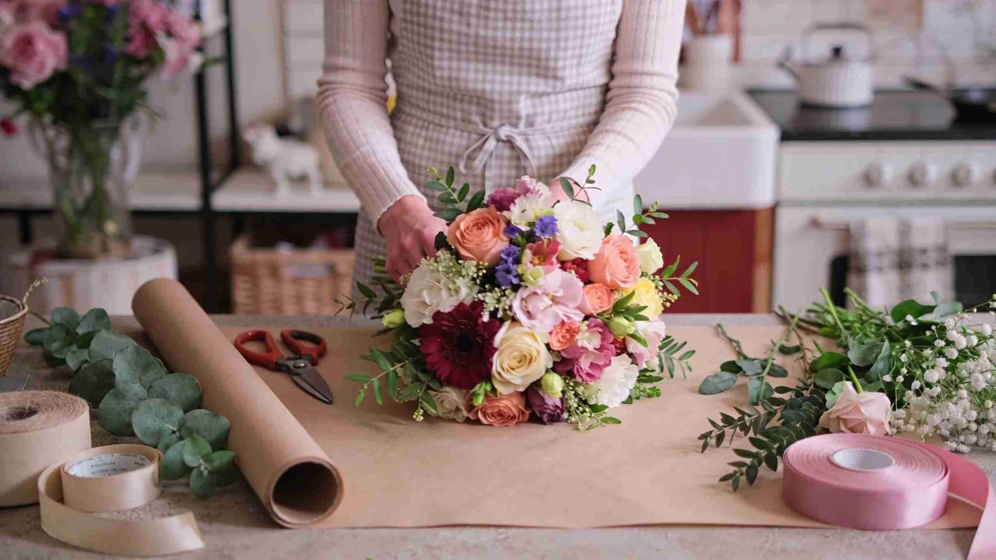 beginner creating a fresh flower bouquet with greenery floral tools wrapping paper and ribbon on a bright home workspace_11zon