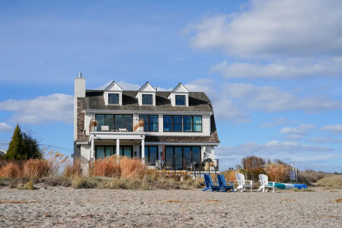 Beachfront house with wooden siding and large windows under blue sky with scattered clouds