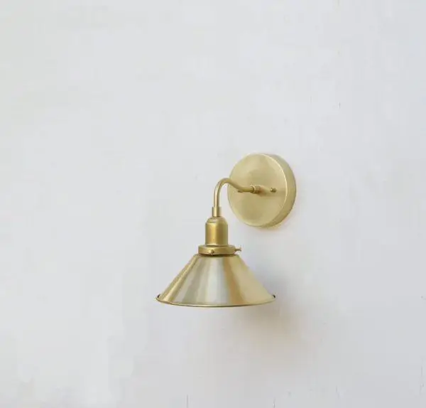 Brass wall sconce with cone-shaped shade mounted on white wall