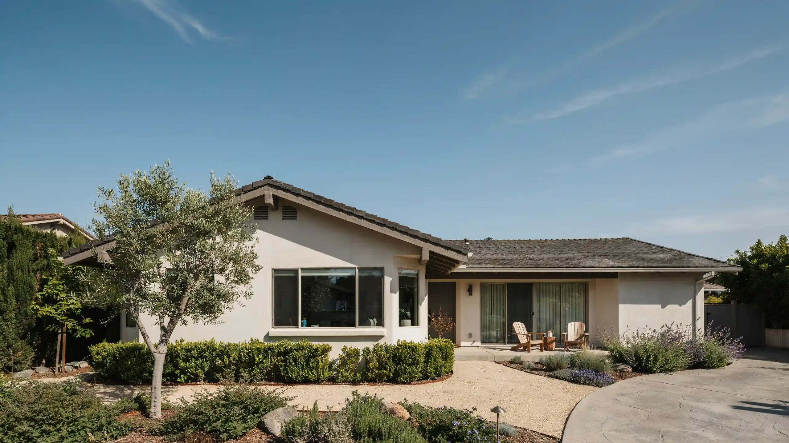 Single-story rambler house with a gray tile roof, surrounded by drought-tolerant landscaping and a paved driveway.