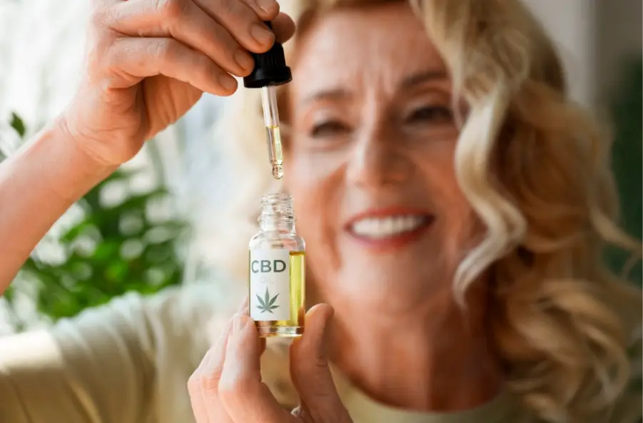 Person holding CBD oil dropper with green plant in blurry background